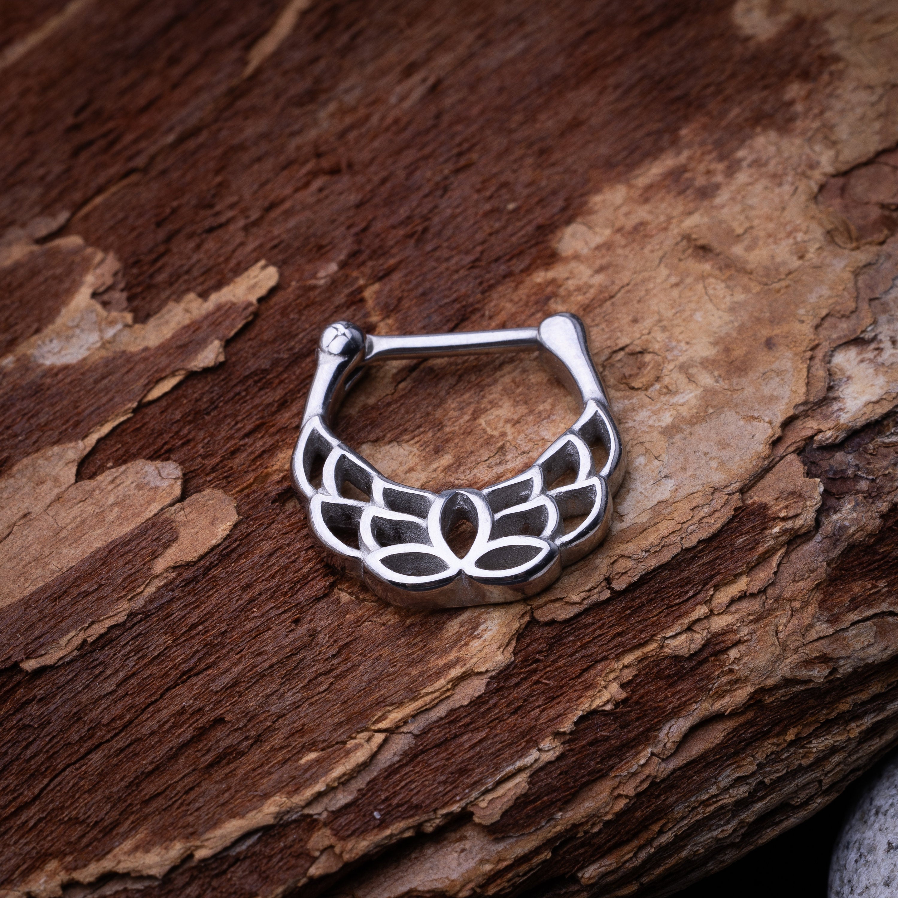 Close-up of a silver septum clicker with a lotus-inspired design, showcasing intricate petal details and a secure hinged clasp on a wooden background.