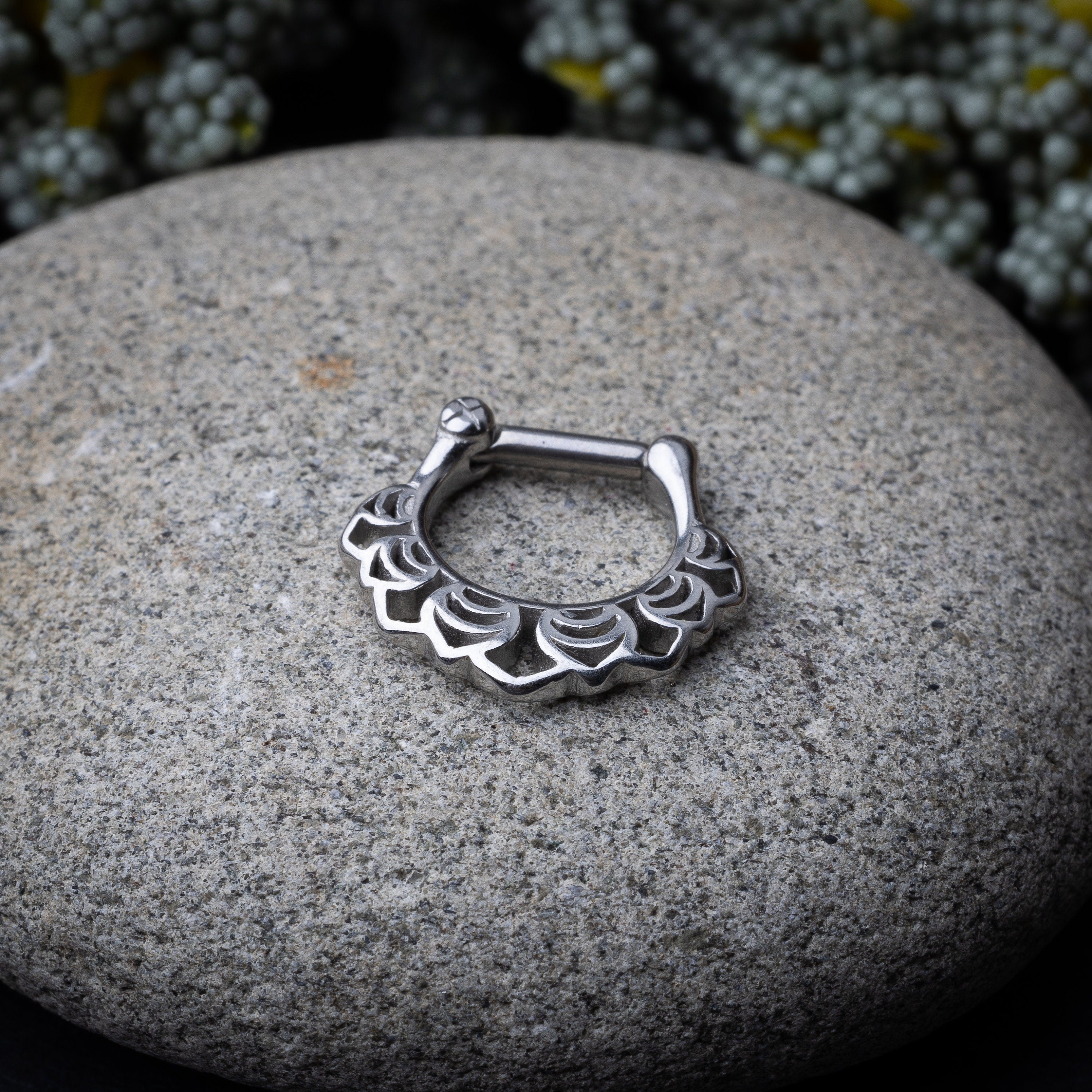 Close-up of a silver septum clicker with an Art Deco-inspired scalloped design, displayed on a stone background with a secure hinged clasp.