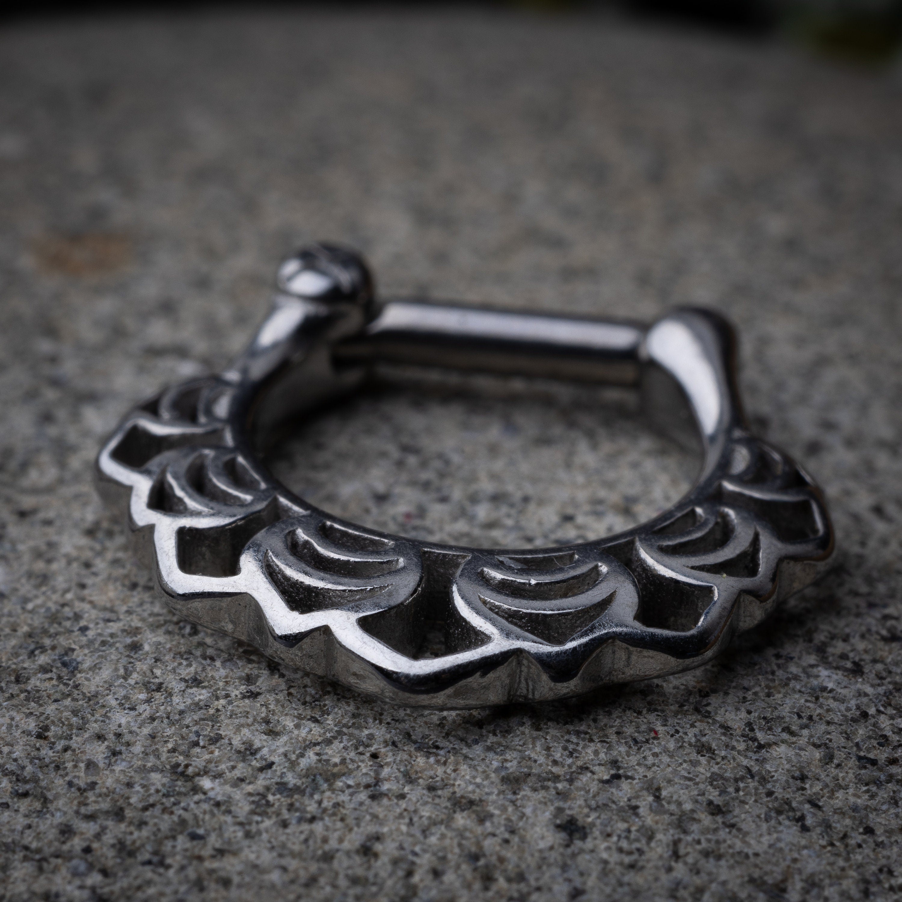 Close-up of a silver septum clicker with an Art Deco-inspired scalloped design, displayed on a dark background with a secure hinged clasp.