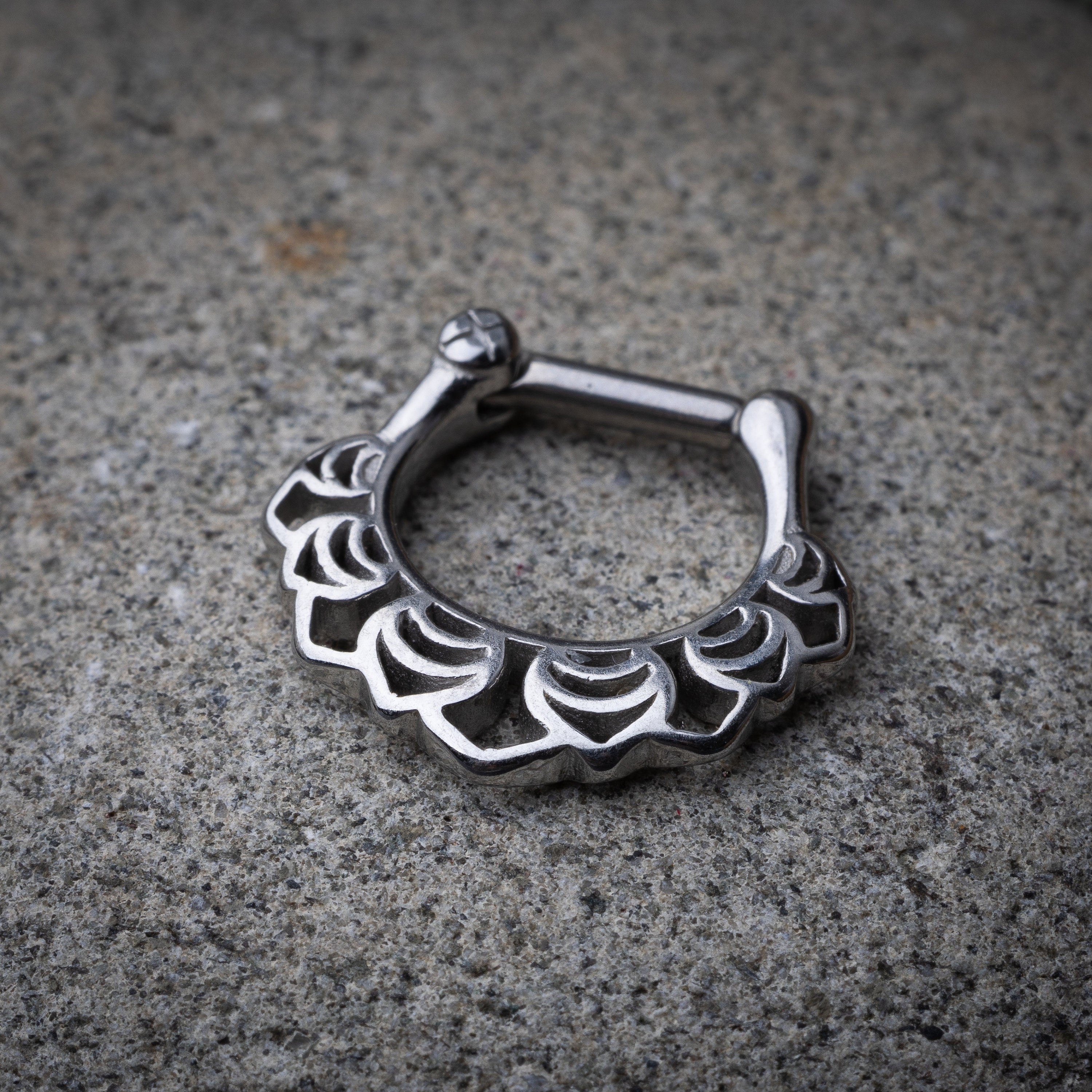Close-up of a silver septum clicker with an Art Deco-inspired scalloped design, displayed on a stone background with a secure hinged clasp.