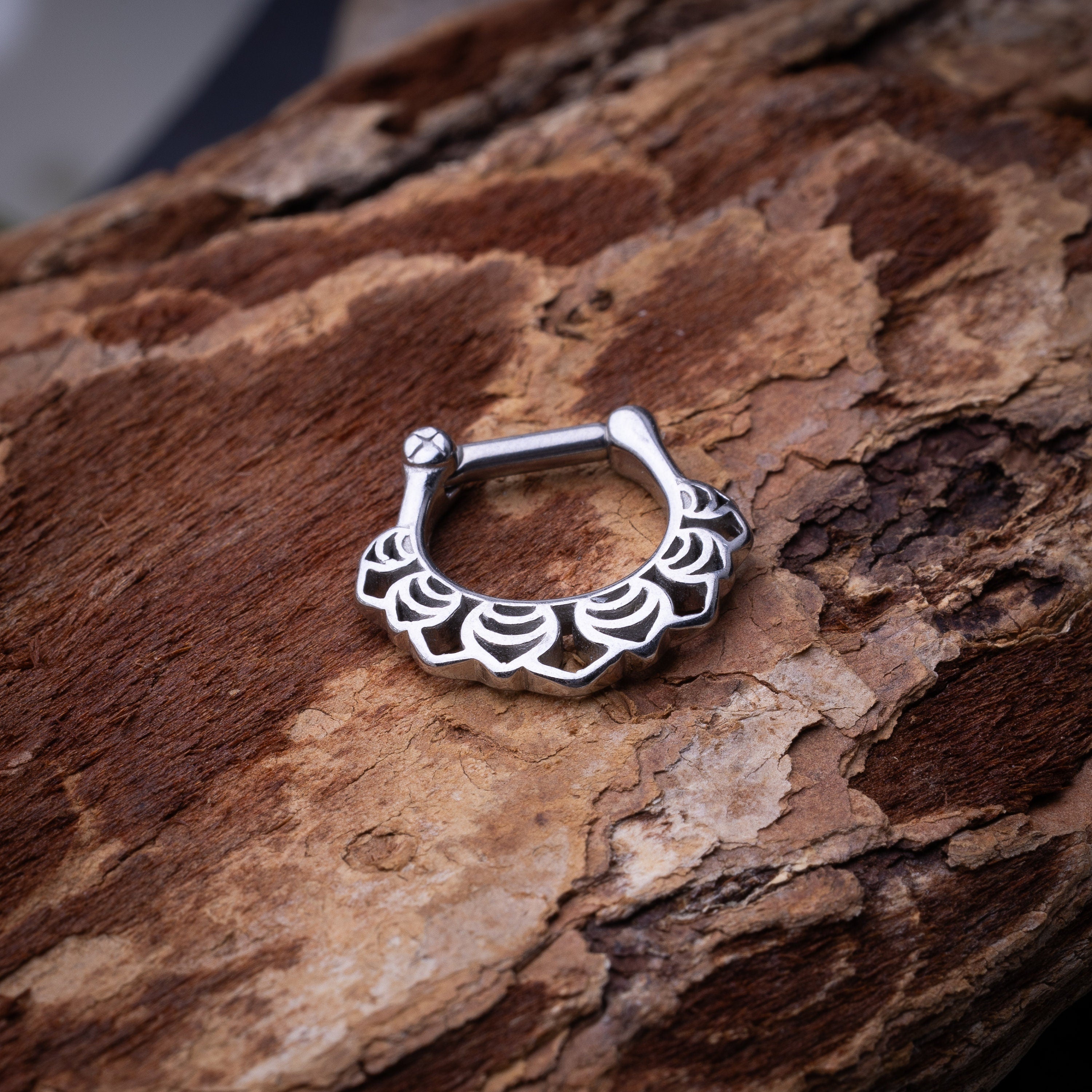 Close-up of a silver septum clicker with an Art Deco-inspired scalloped design, displayed on a wooden background with a secure hinged clasp.