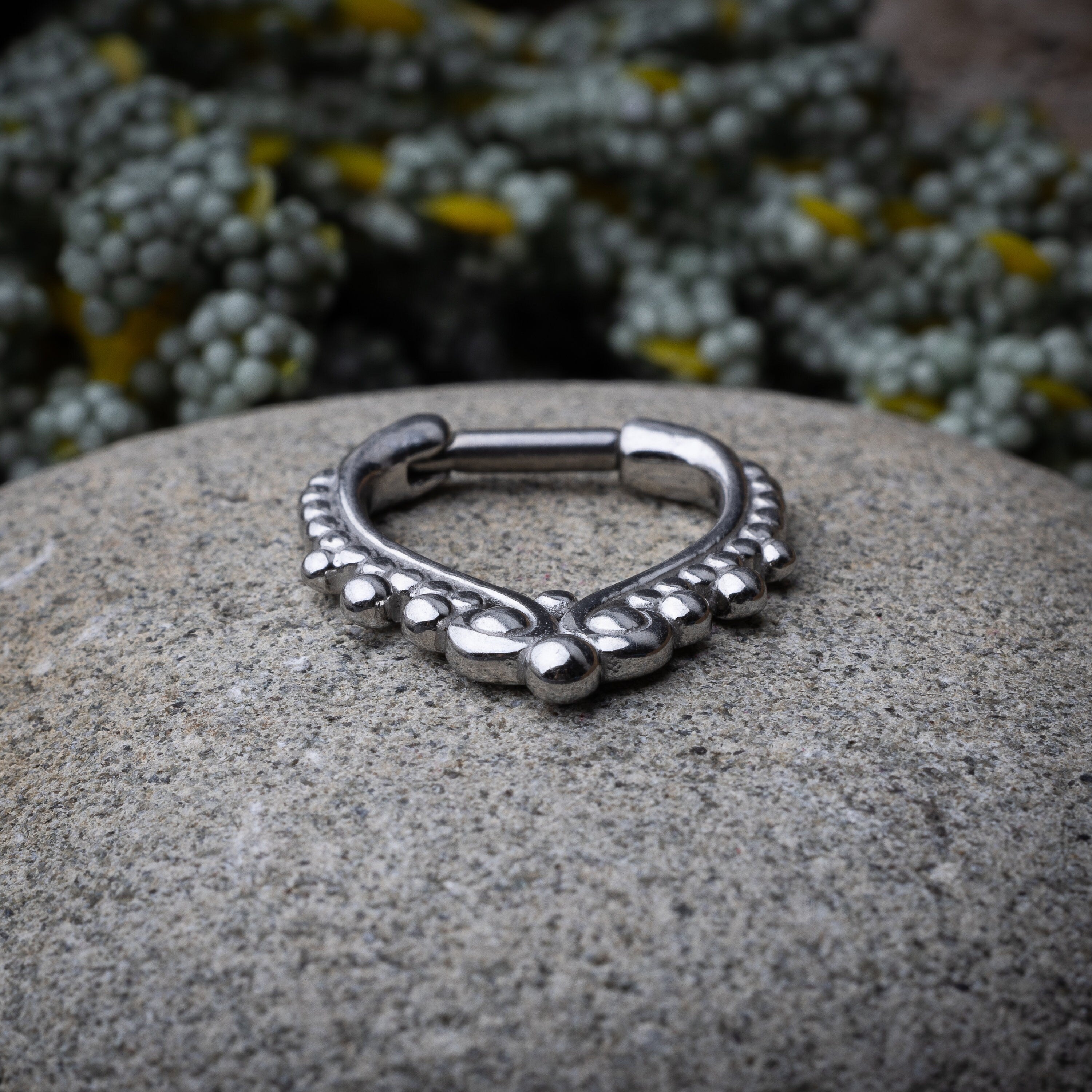 Close-up of a silver septum clicker with a teardrop shape and beaded embellishments, displayed on a Stone background with a secure hinged clasp.