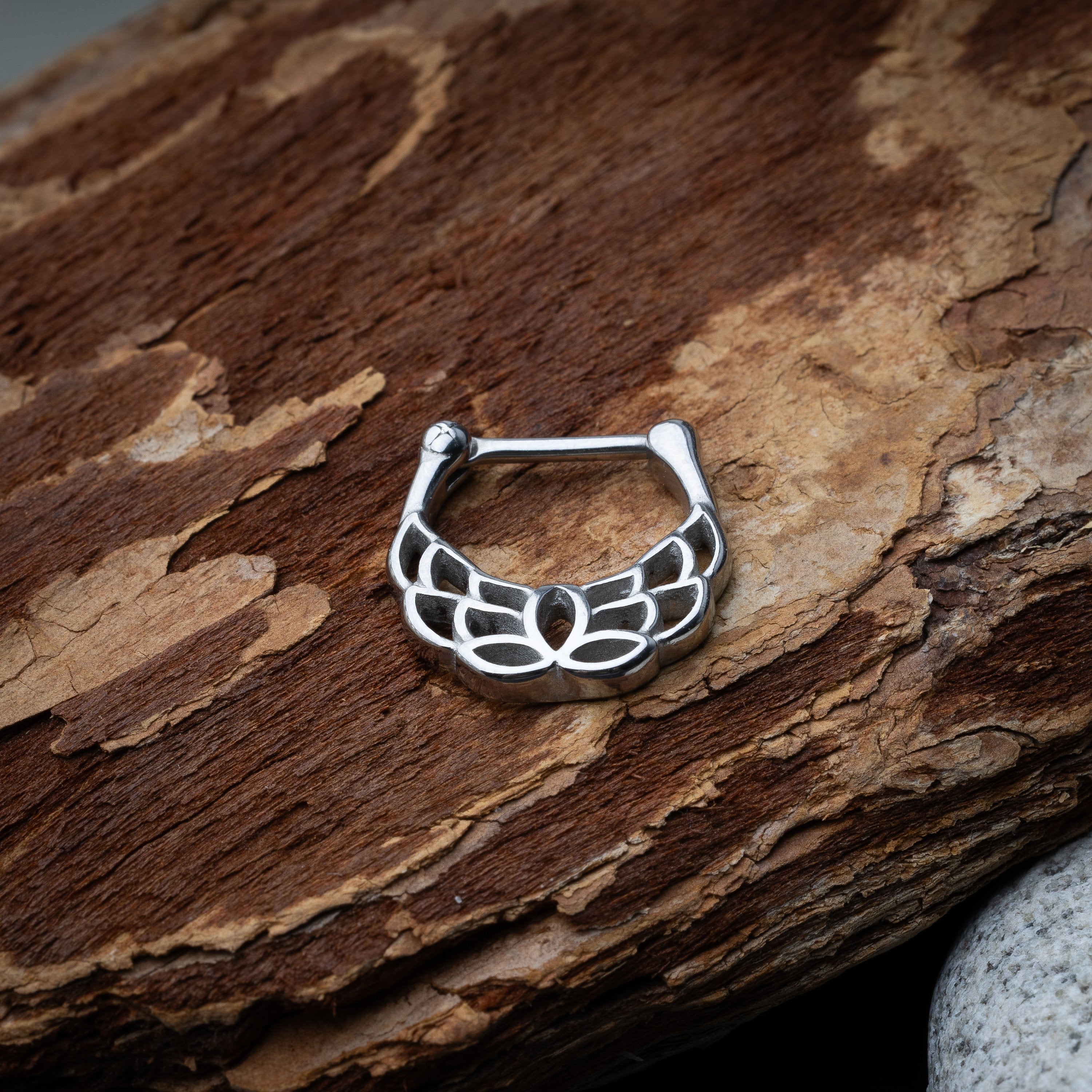 Close-up of a silver septum clicker with a lotus-inspired design, showcasing intricate petal details and a secure hinged clasp on a wooden background.