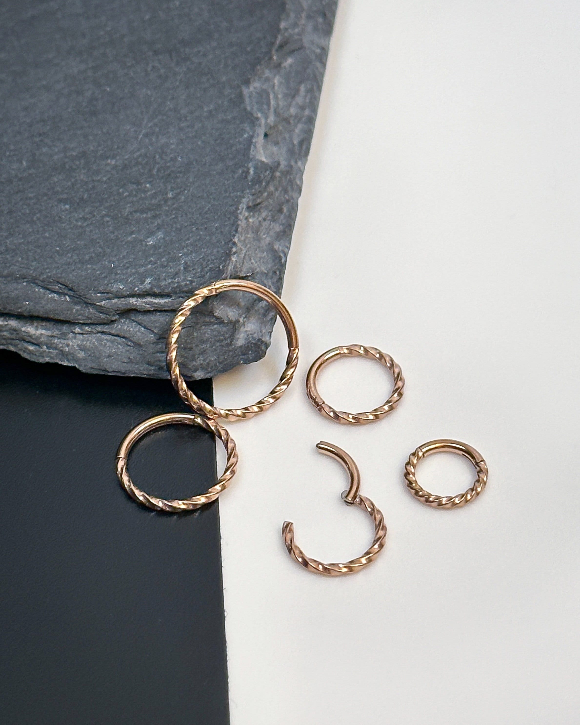 Close-up of a gold hinged ring with a twisted rope design, displayed on a white and black background