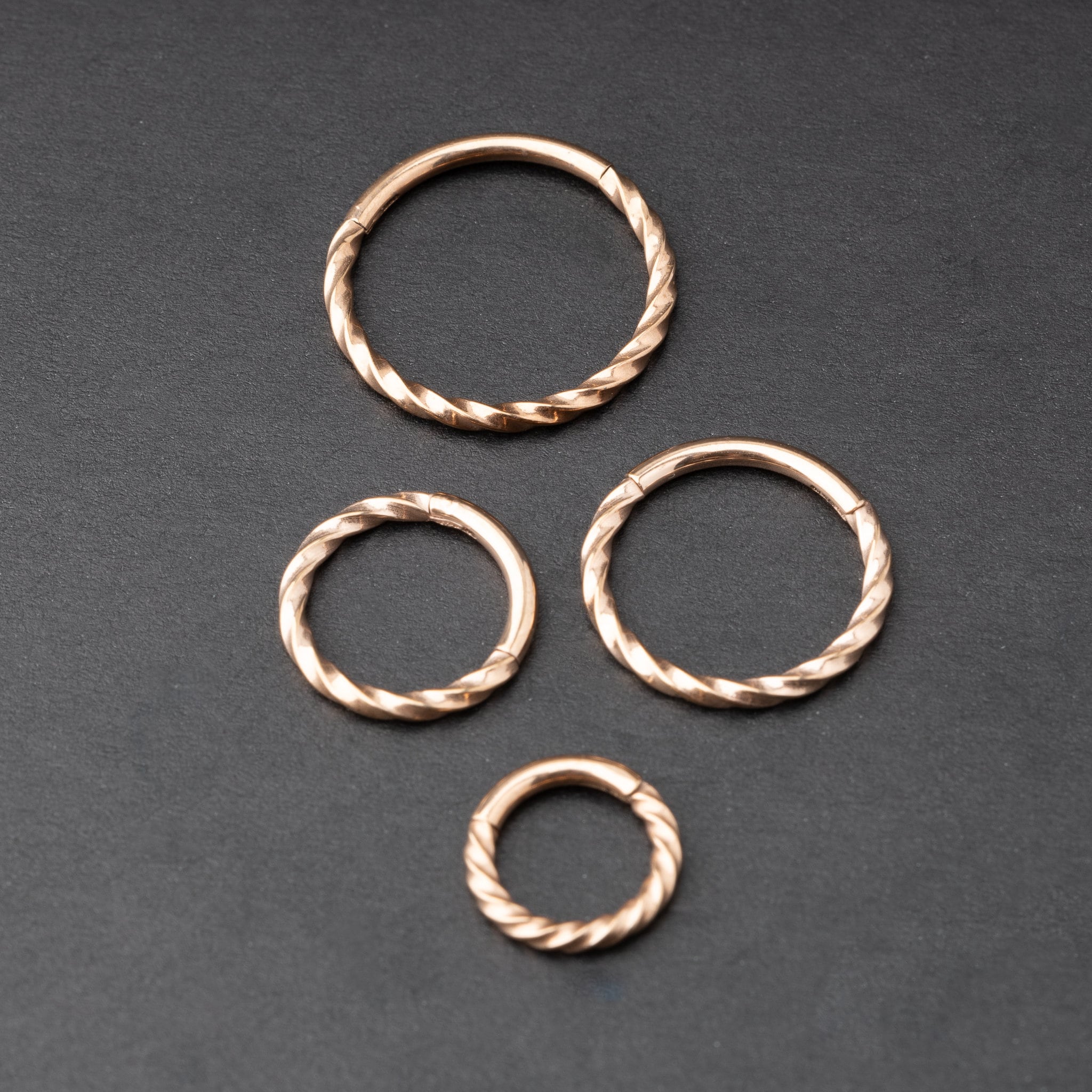 Close-up of a gold hinged ring with a twisted rope design, displayed on a dark background