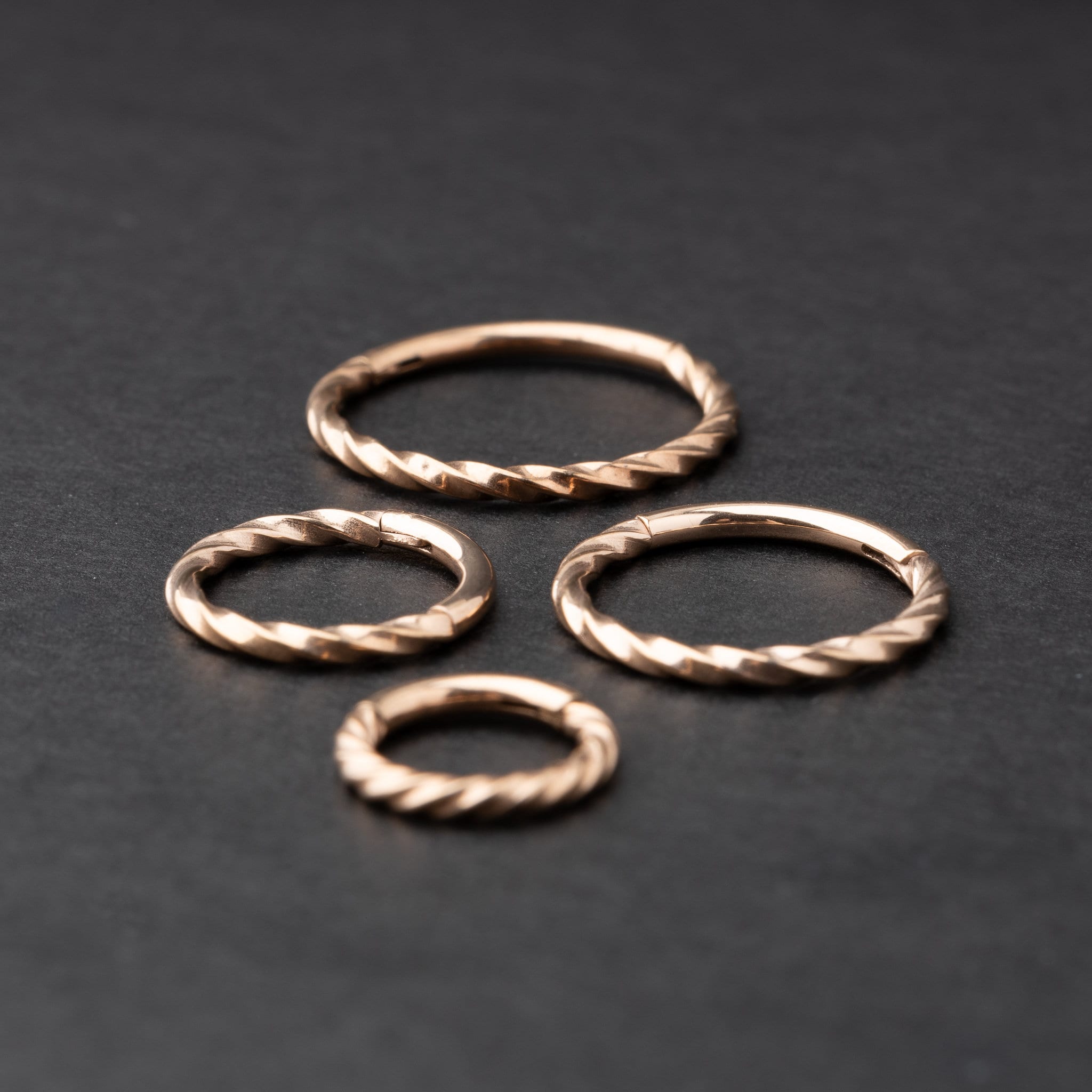 Close-up of a gold hinged ring with a twisted rope design, displayed on a dark background