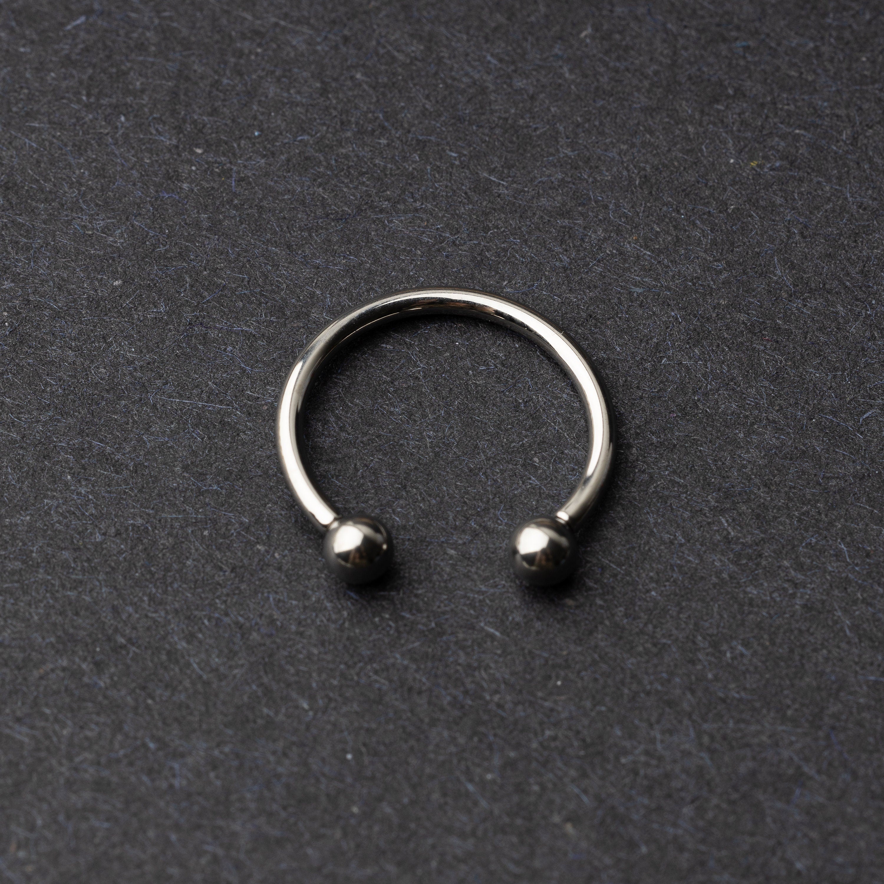 Titanium horseshoe ring with ball ends, displayed on a dark textured background.