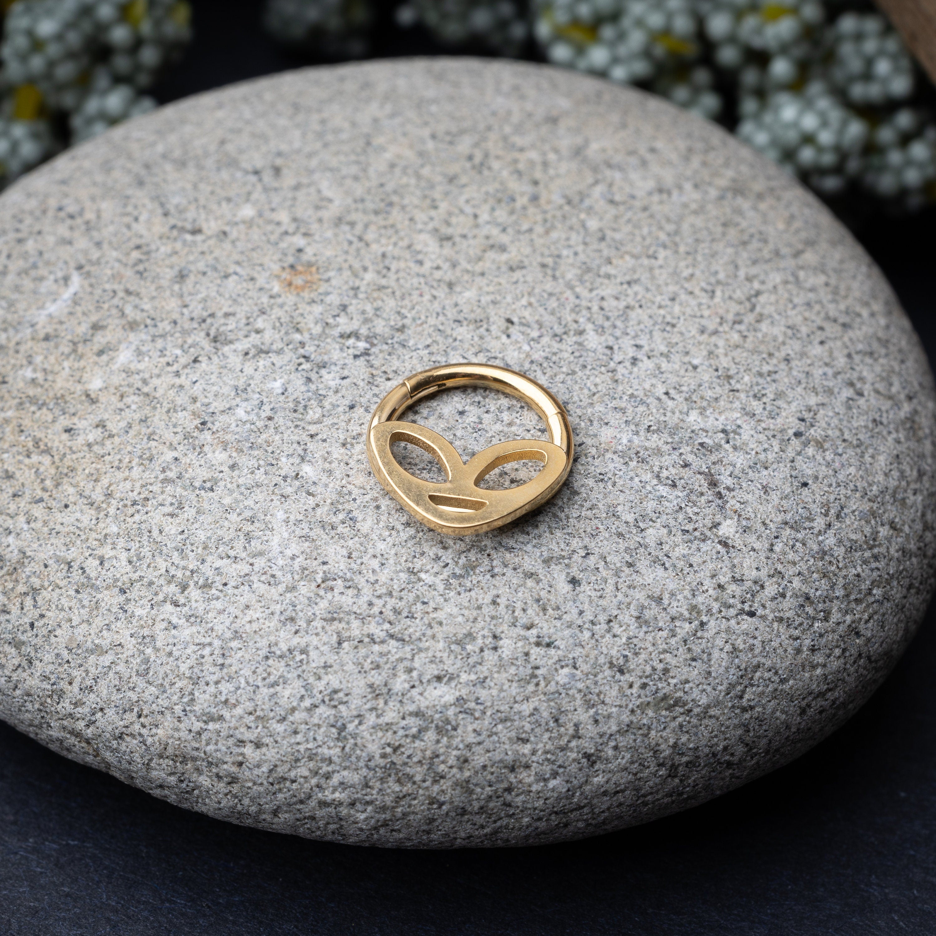 Alien-themed septum clicker in Gold finish, displayed on a stone background.