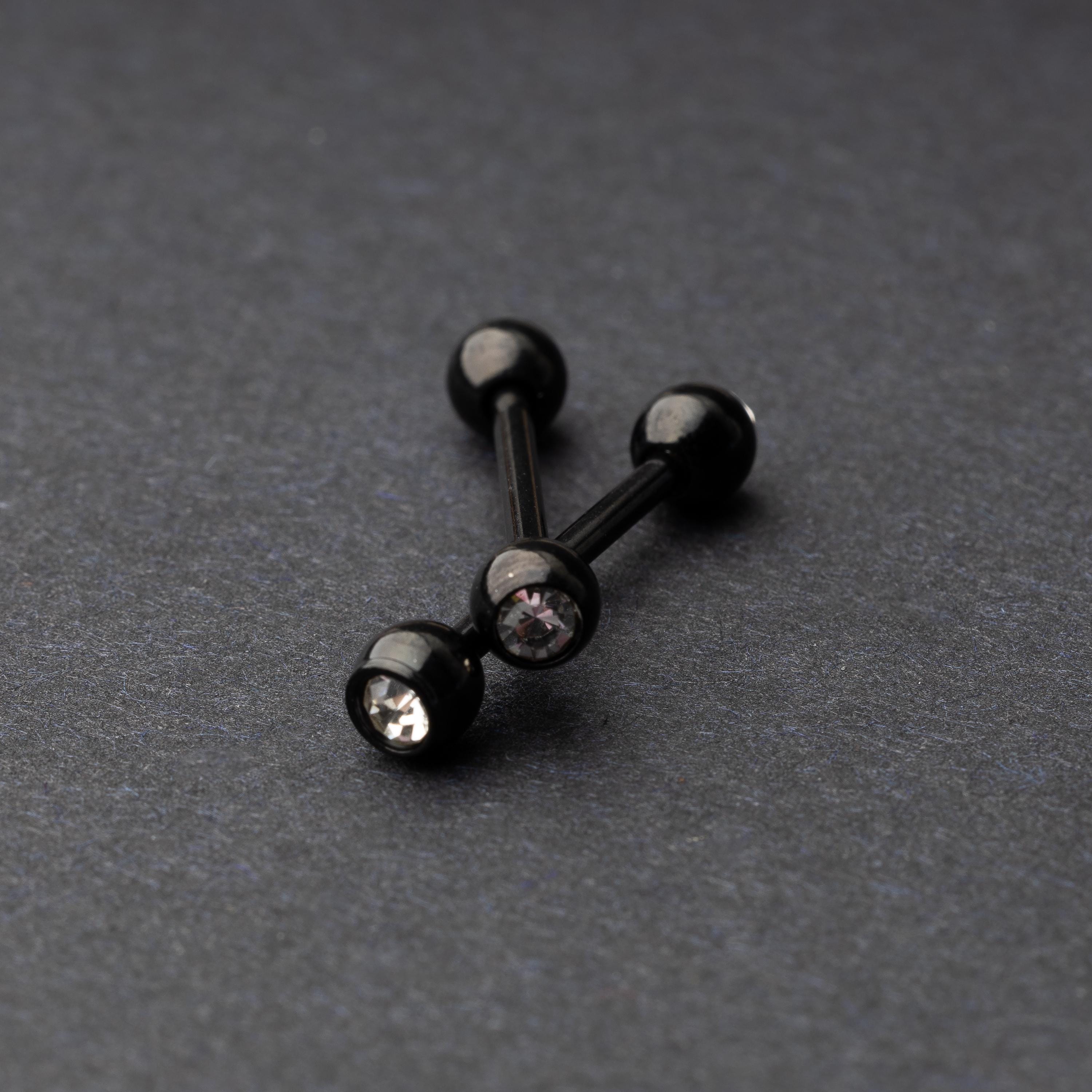 A set of black stainless steel nipple bars with polished gem-studded ends, displayed on a dark background.