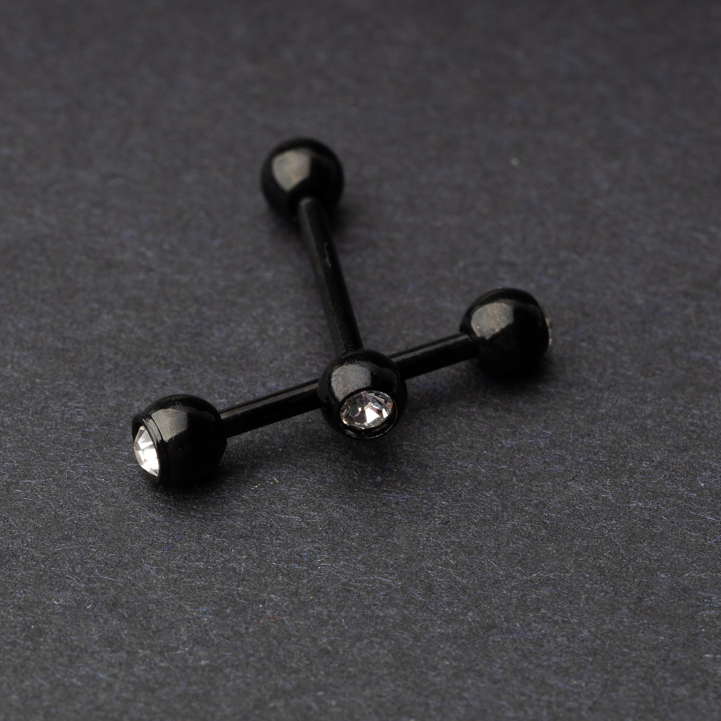 A set of black stainless steel nipple bars with polished gem-studded ends, displayed on a dark background.