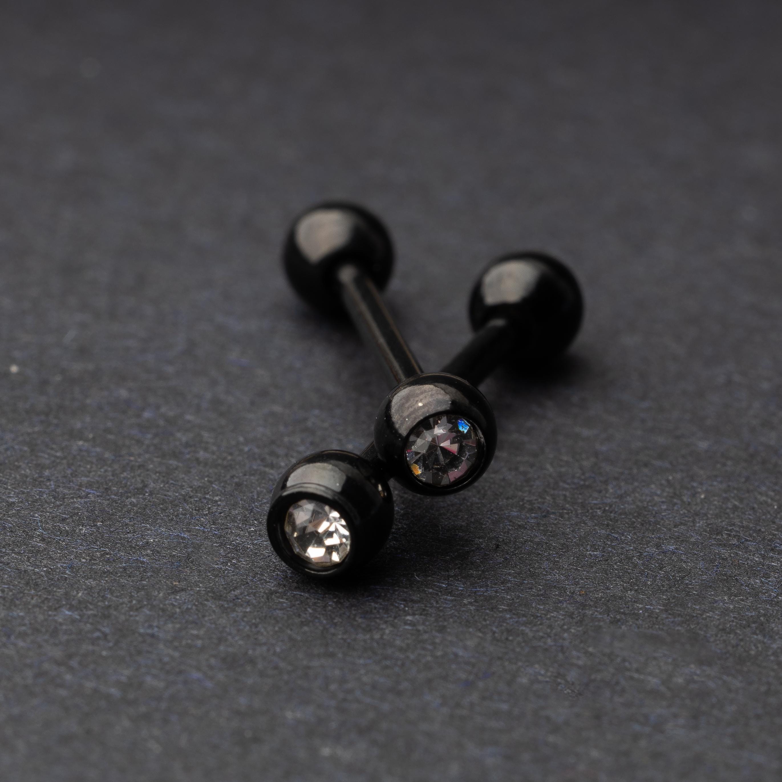 A set of black stainless steel nipple bars with polished gem-studded ends, displayed on a dark background.