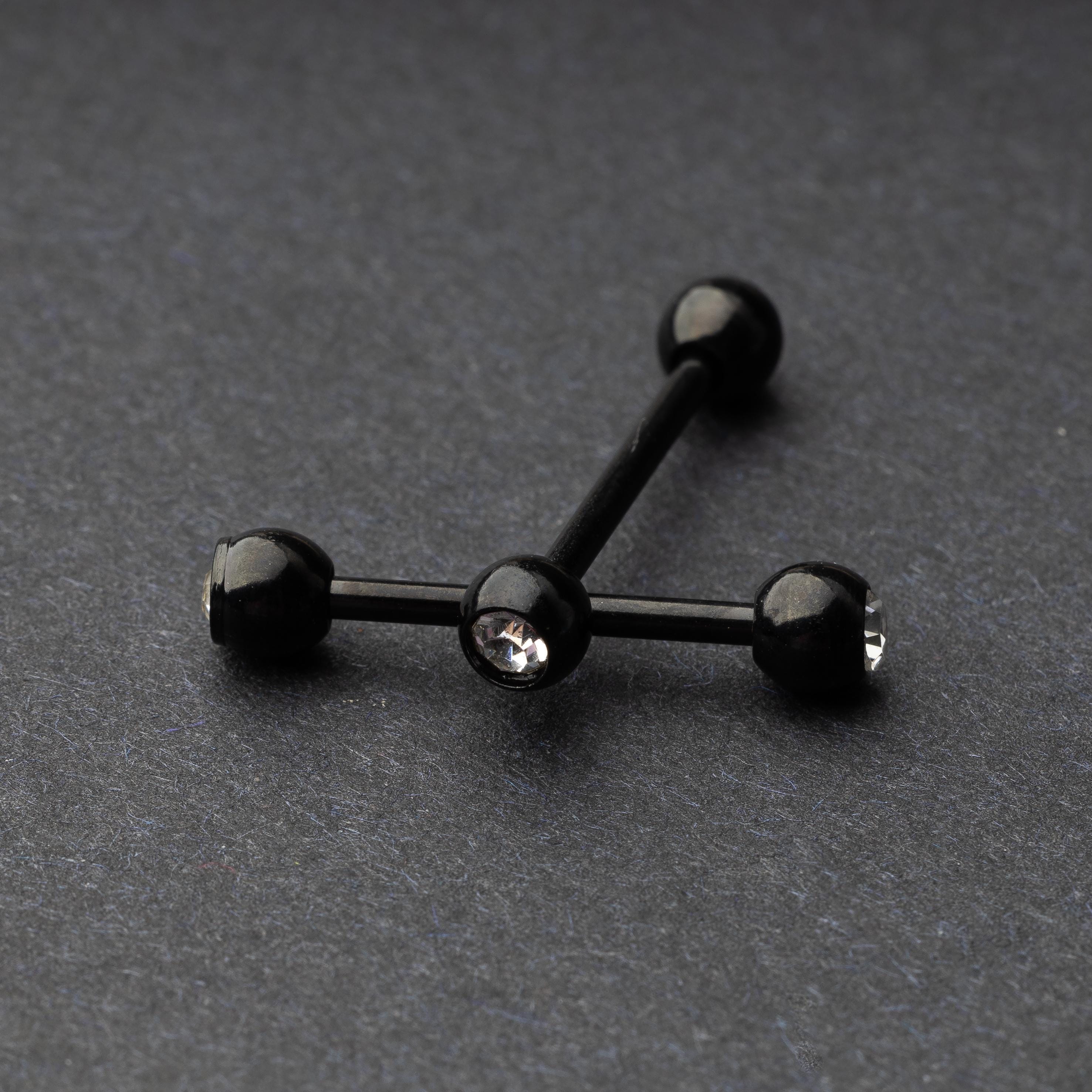 A set of black stainless steel nipple bars with polished gem-studded ends, displayed on a dark background.