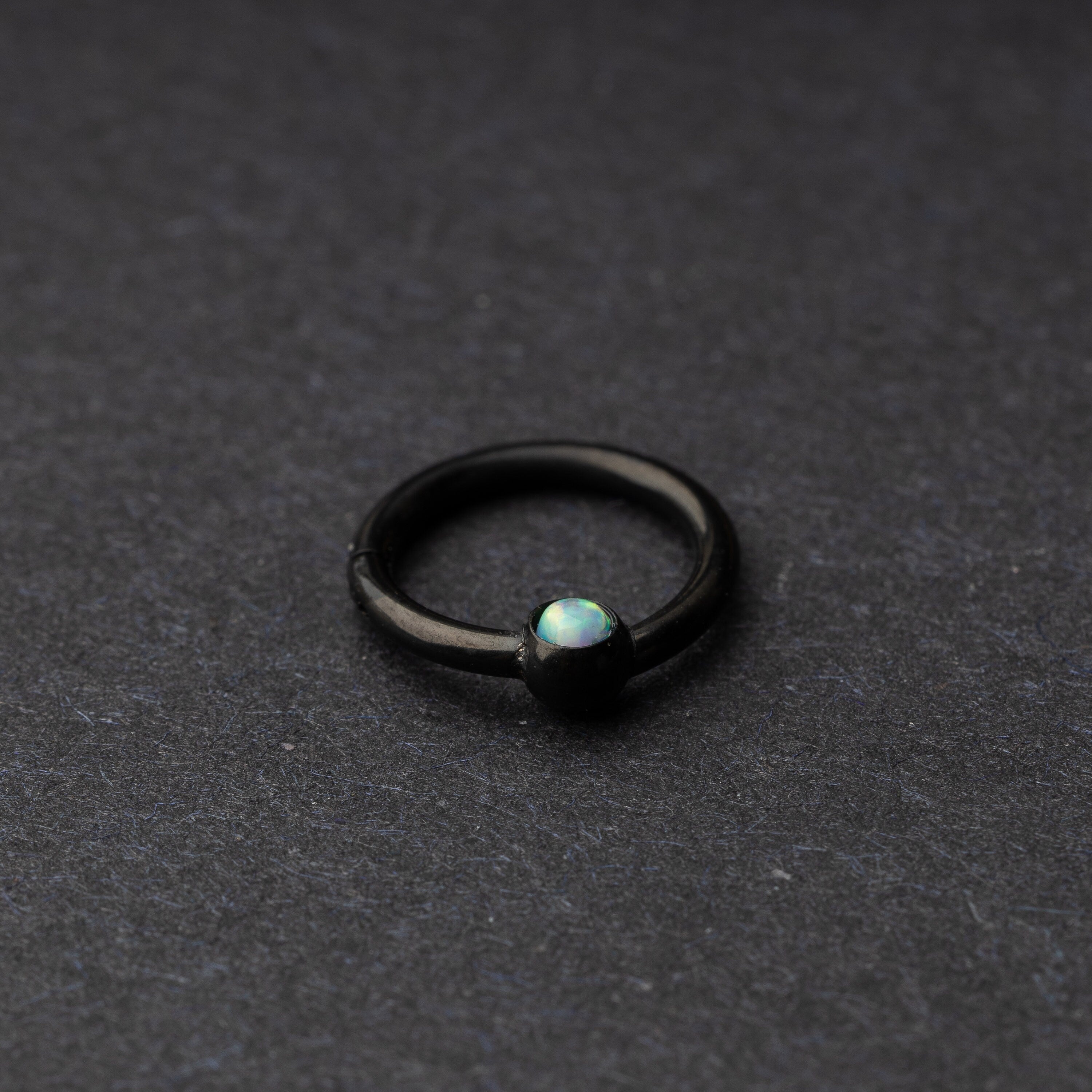 Seamless clicker in black featuring an opalescent bead, displayed on a dark background.