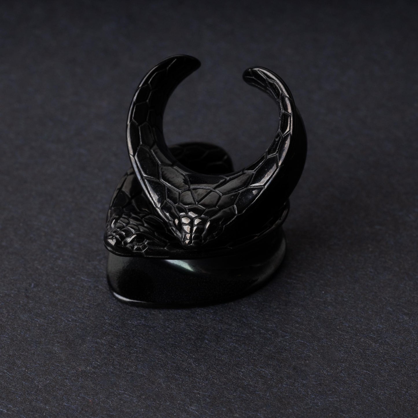 A pair of snakehead saddle tunnels for stretched ears in black, displayed on a dark background.