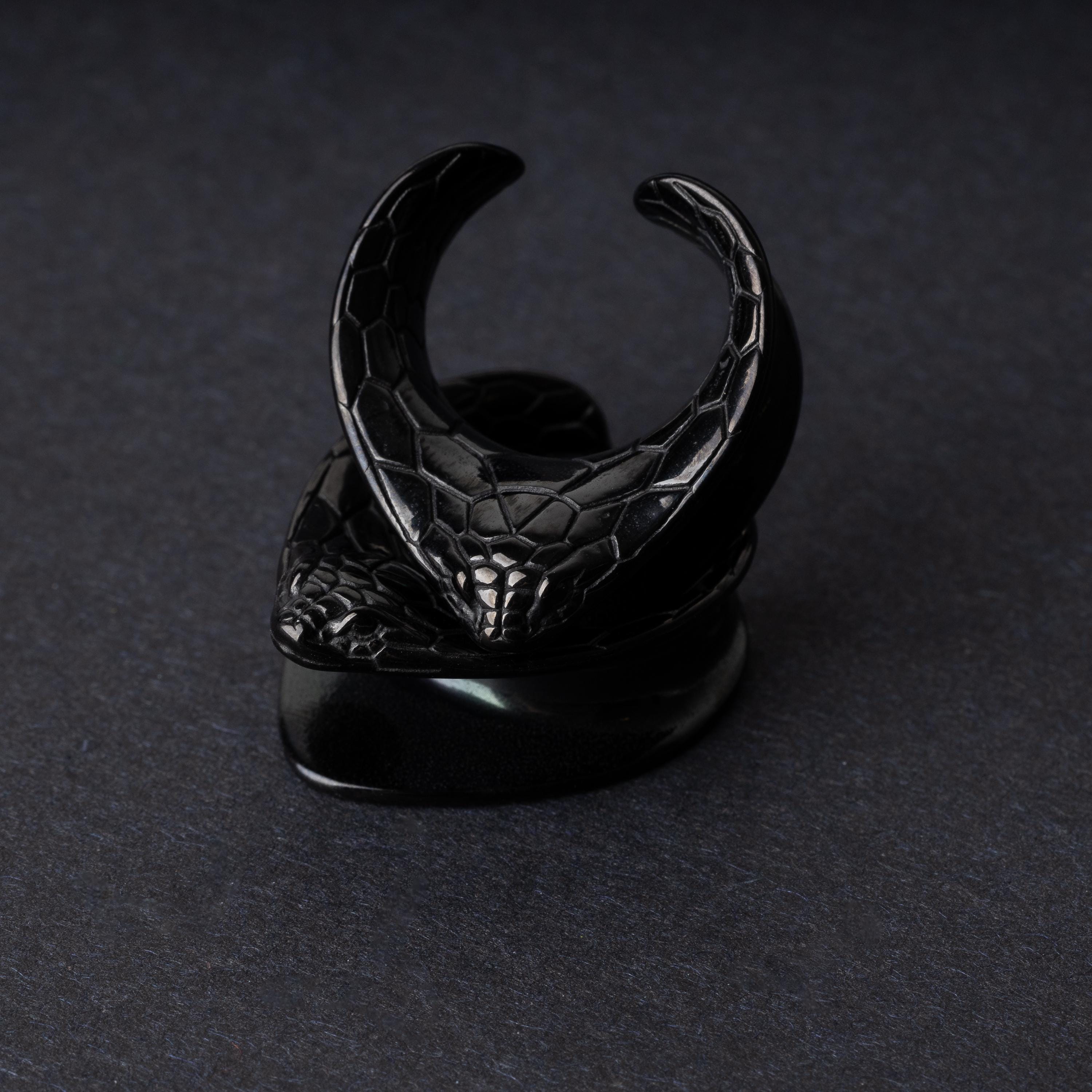 A pair of snakehead saddle tunnels for stretched ears in black, displayed on a dark background.