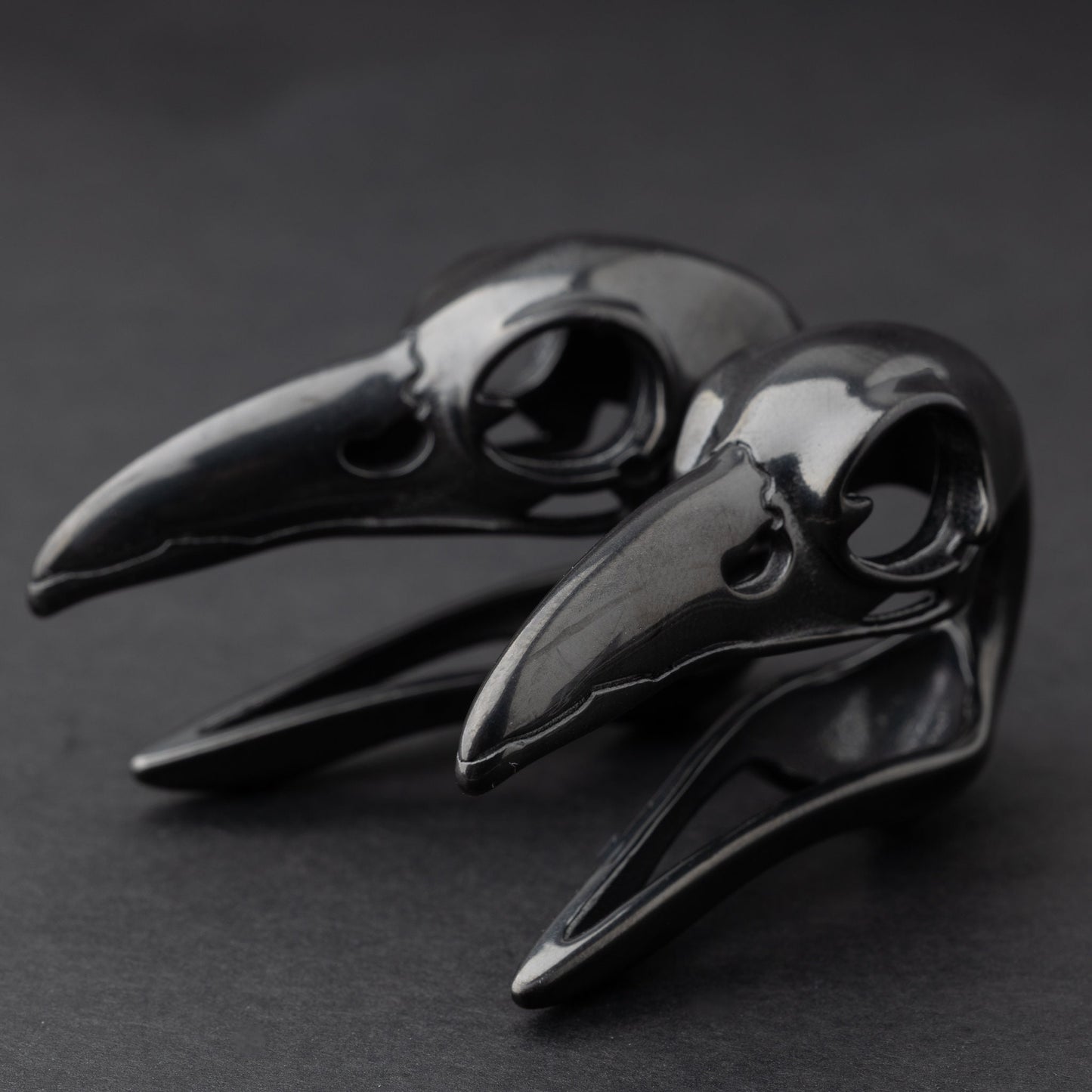 Raven skull saddle plugs in black, elegantly displayed on a dark background.