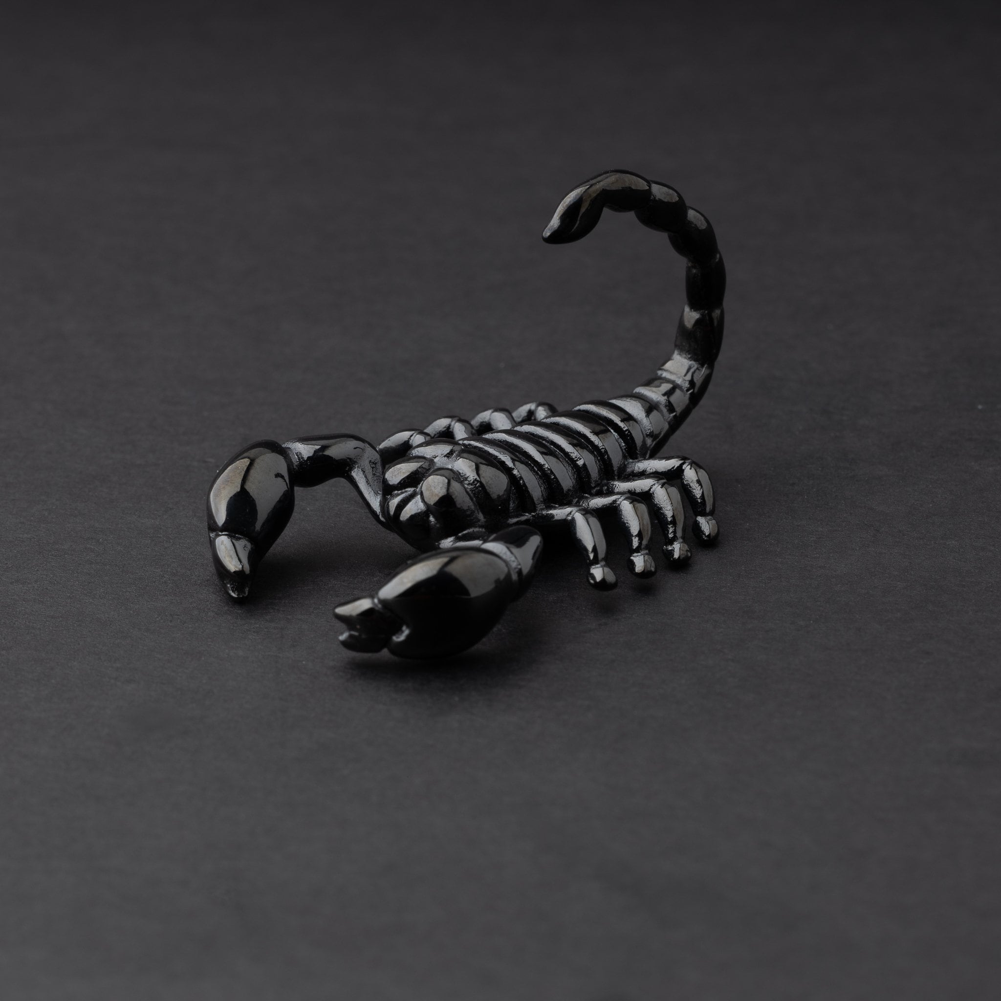 Scorpion-shaped ear hanger in black displayed on a dark matte background, highlighting their detailed and edgy design.