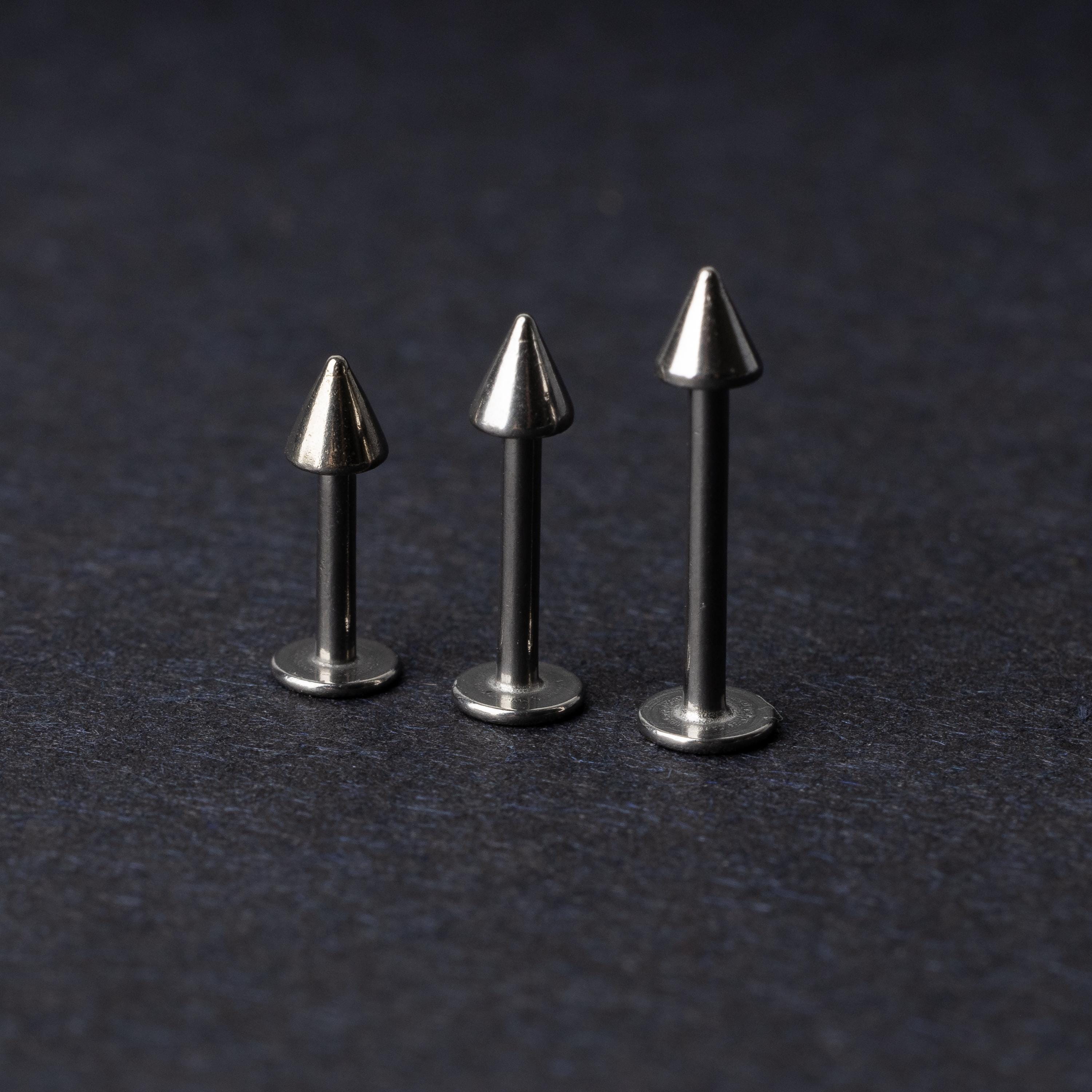 Three stainless steel flat-back barbells with spiked ends, displayed on a dark background showcasing their polished and sleek design.