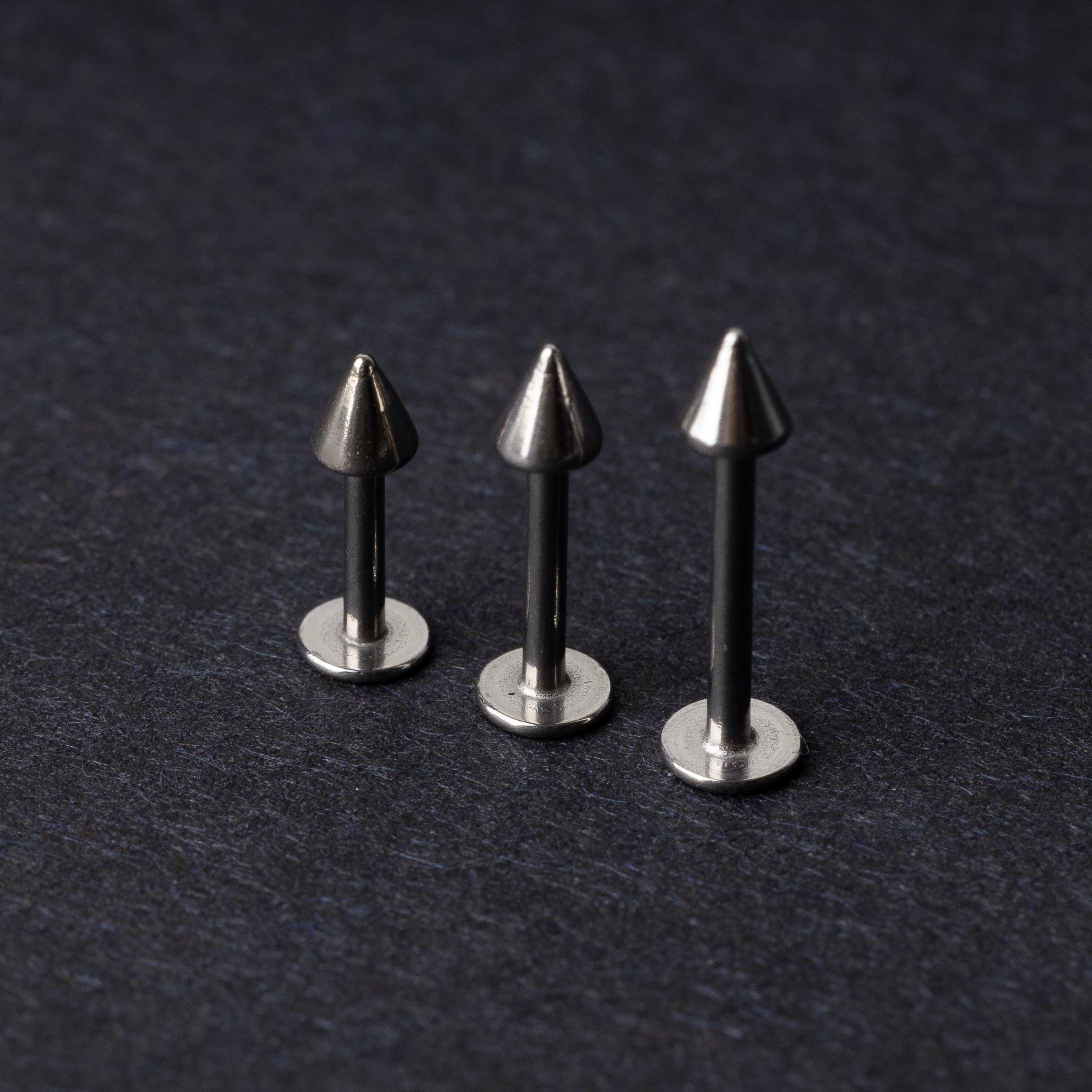 Three stainless steel flat-back barbells with spiked ends, displayed on a dark background showcasing their polished and sleek design.
