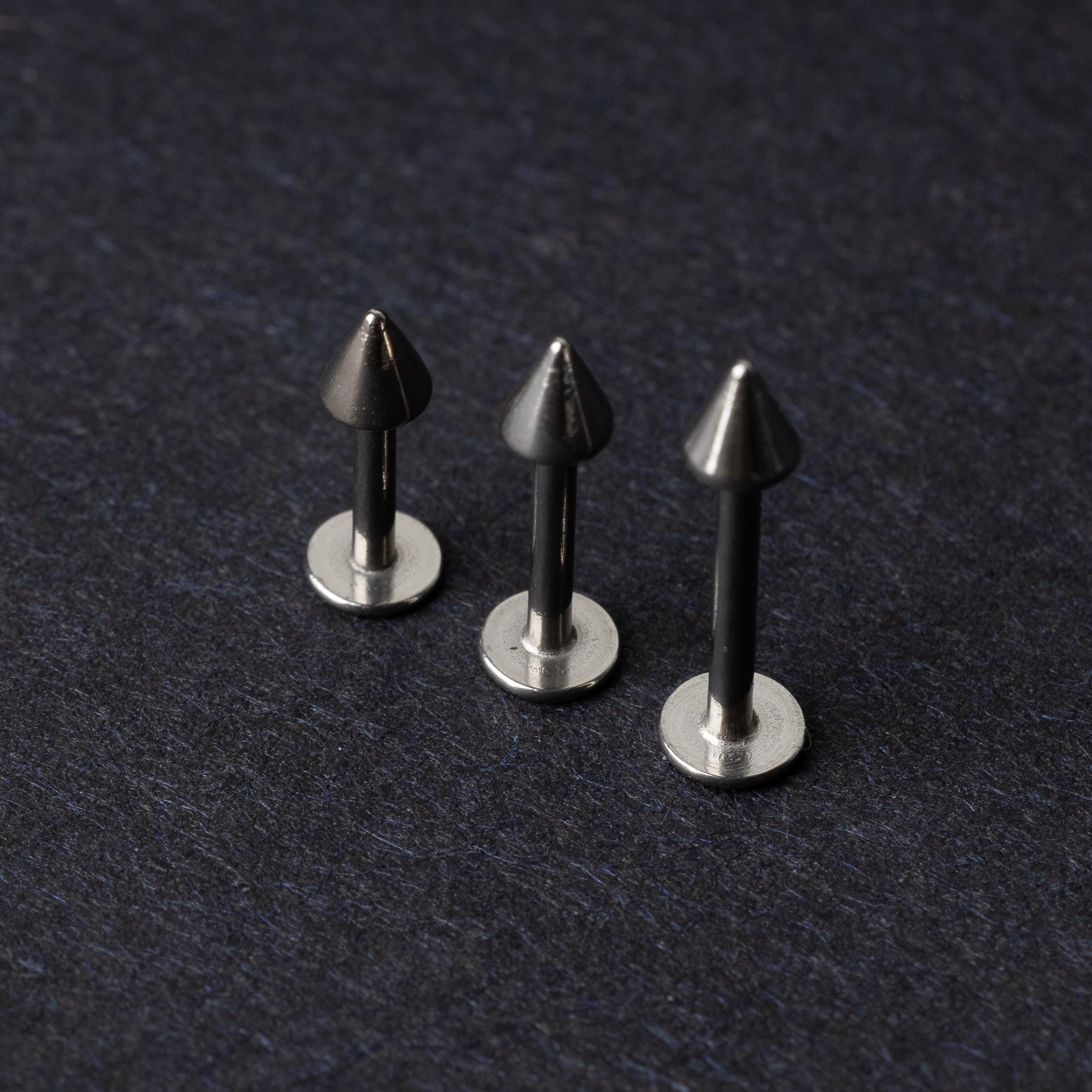 Three stainless steel flat-back barbells with spiked ends, displayed on a dark background showcasing their polished and sleek design.