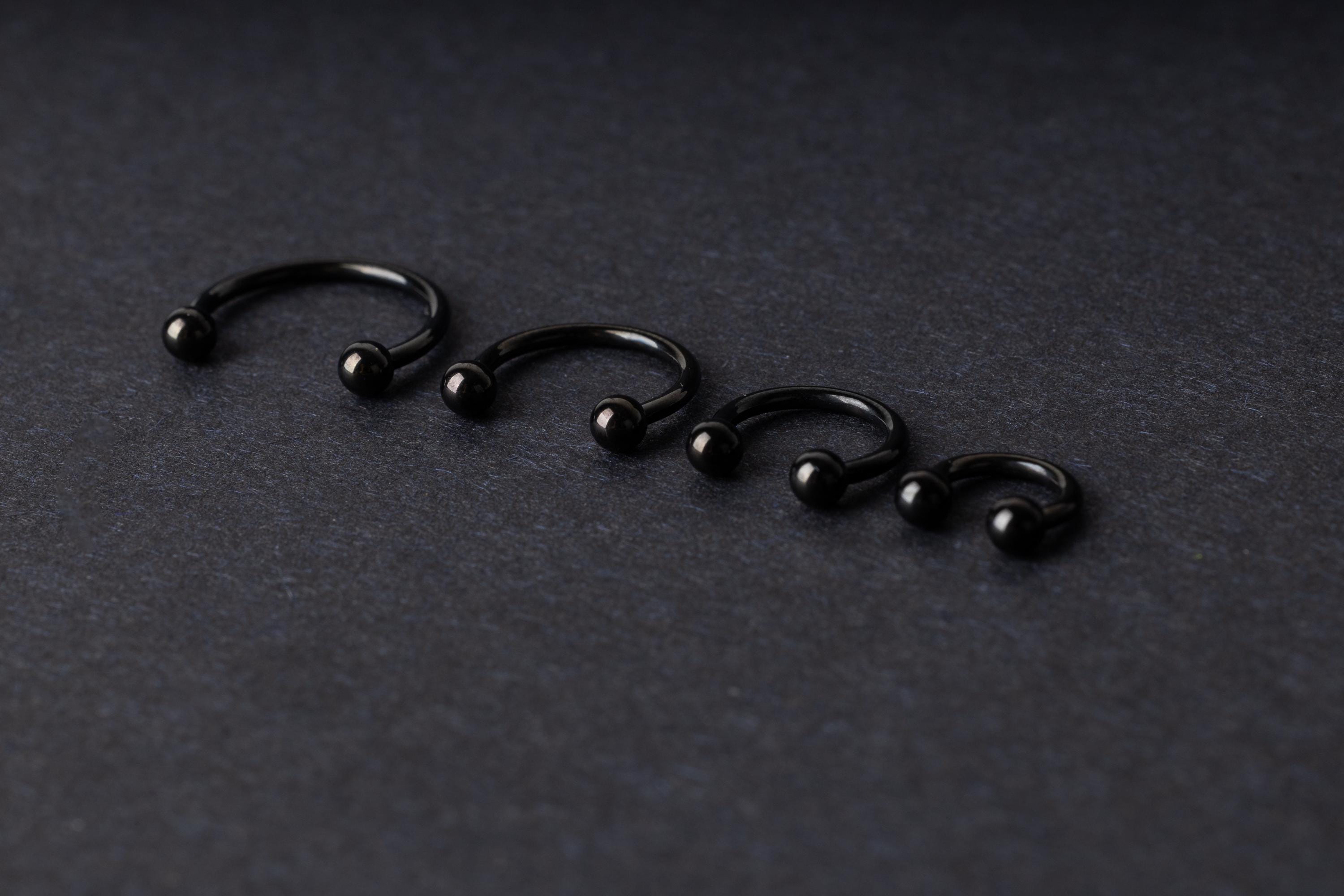 four G23 titanium black horseshoe rings with ball ends in varying sizes, displayed on a dark background showcasing their polished finish.