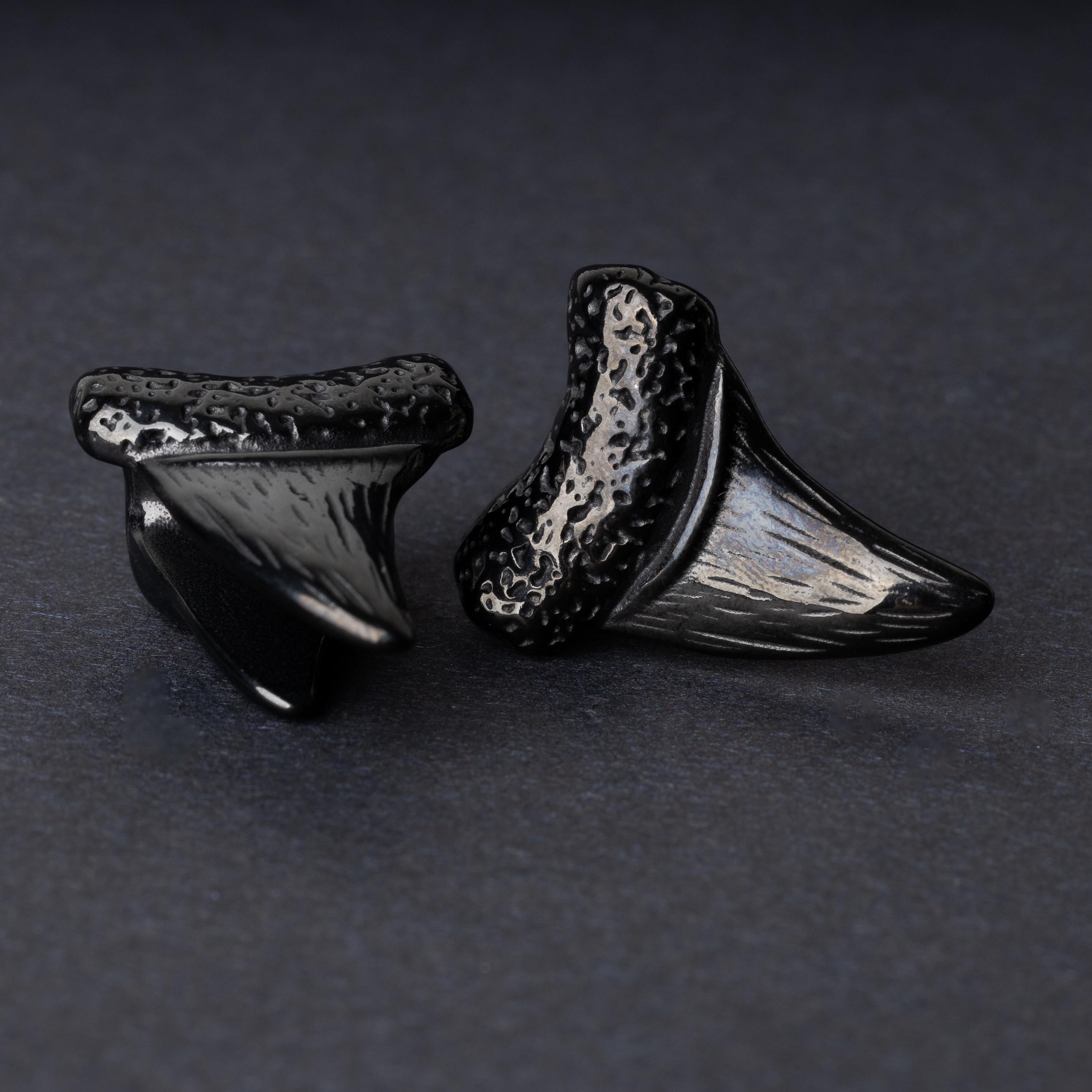 Close-up of black tooth ear weights featuring textured detailing, displayed on a dark background.