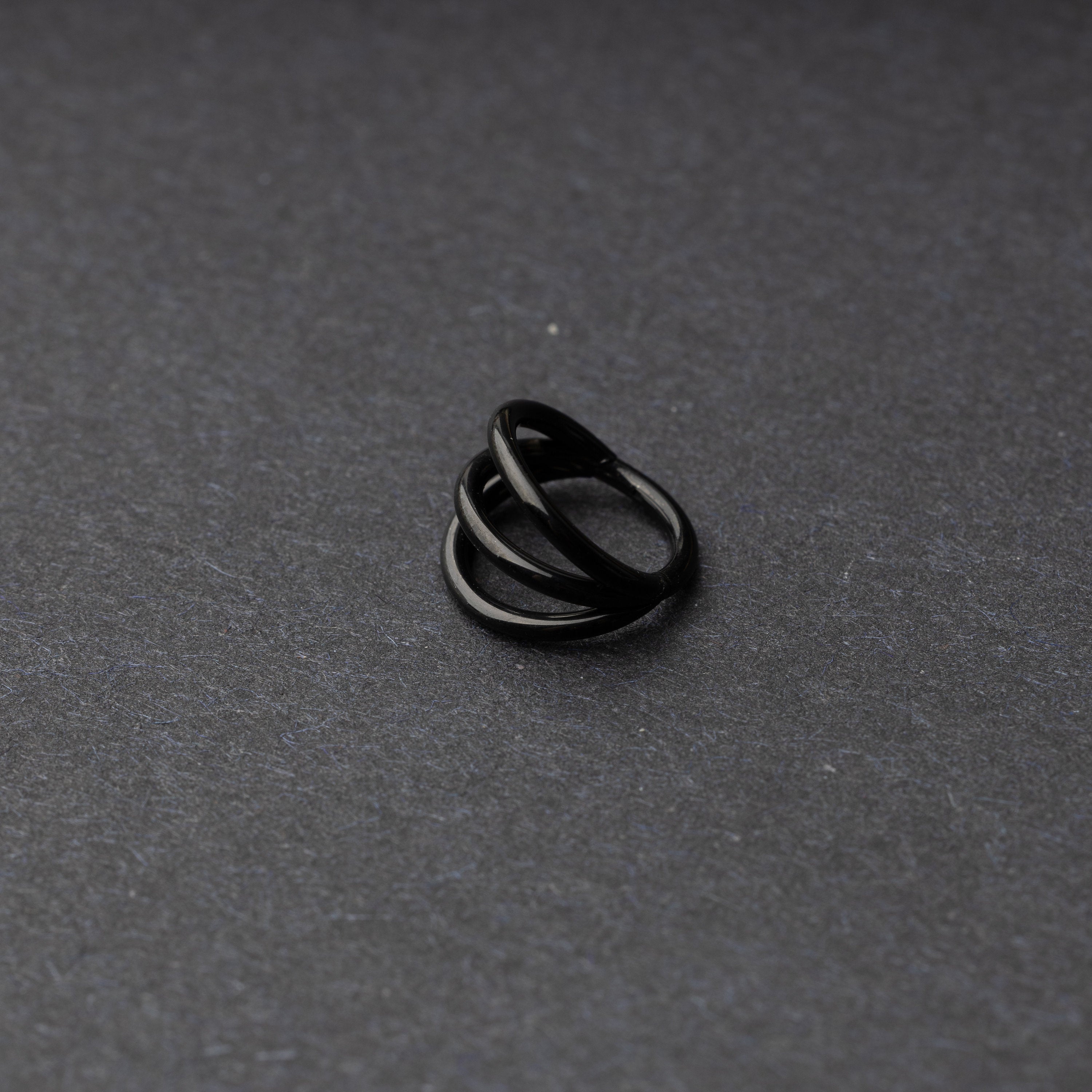 Four triple-band hoop septum clicker ring in black finish, displayed on a dark background.