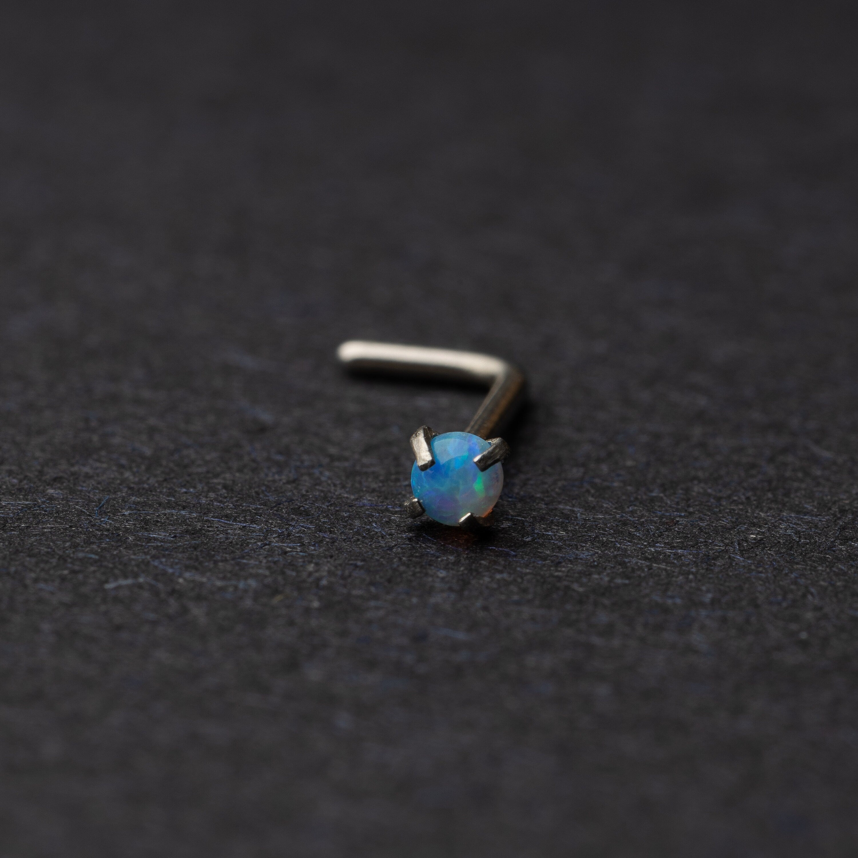 Opal L shaped nose stud on a dark background
