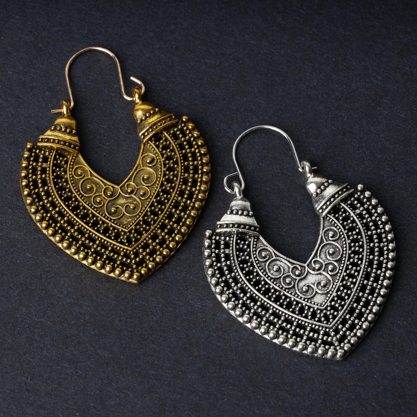 Pair of earrings in antique gold and silver finishes with intricate patterns and textured detailing, displayed on a dark background.