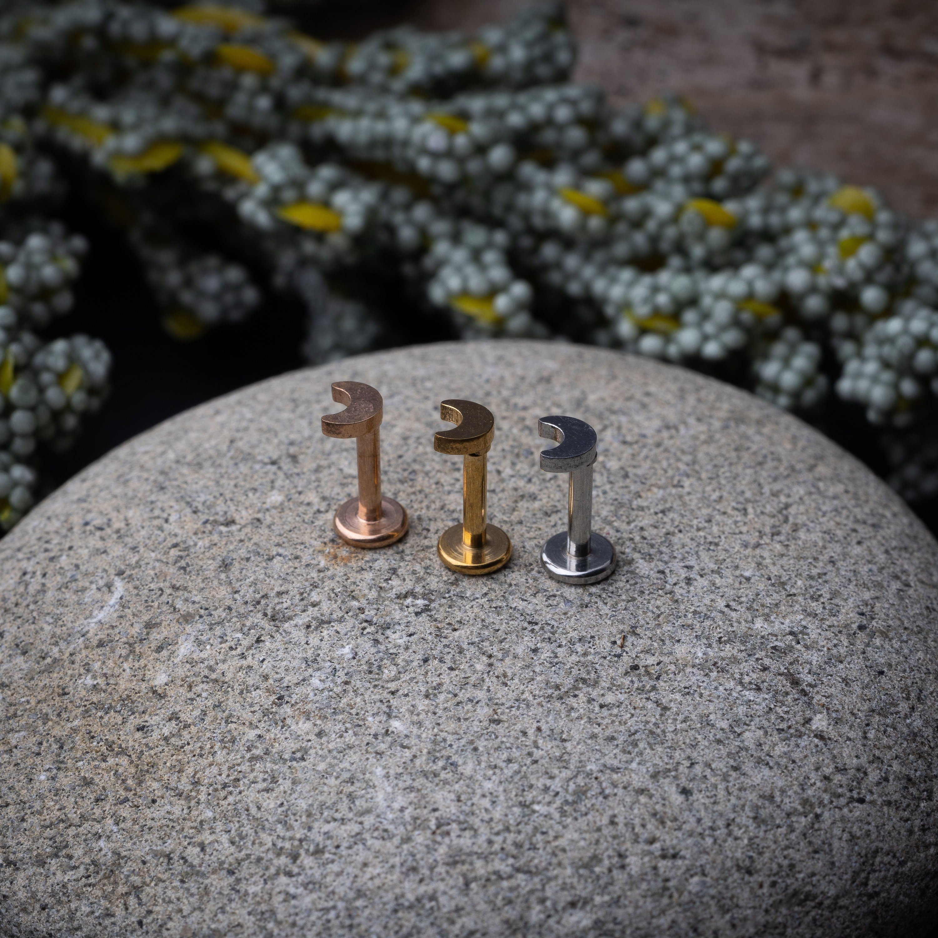 Gold, silver, and rose gold crescent moon labret studs displayed on a stone background