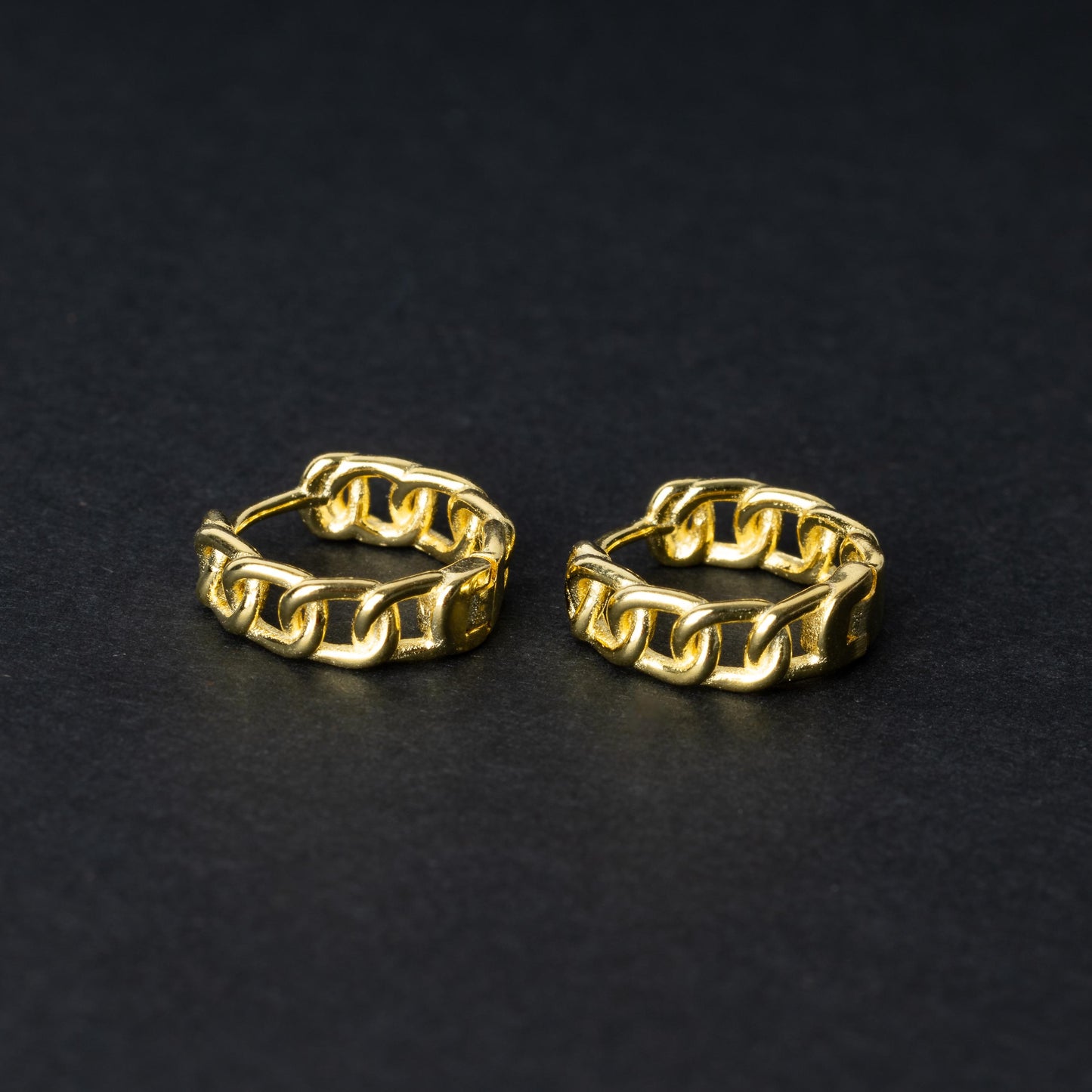 Gold hoop earrings with a chain-link design, displayed on a dark background.