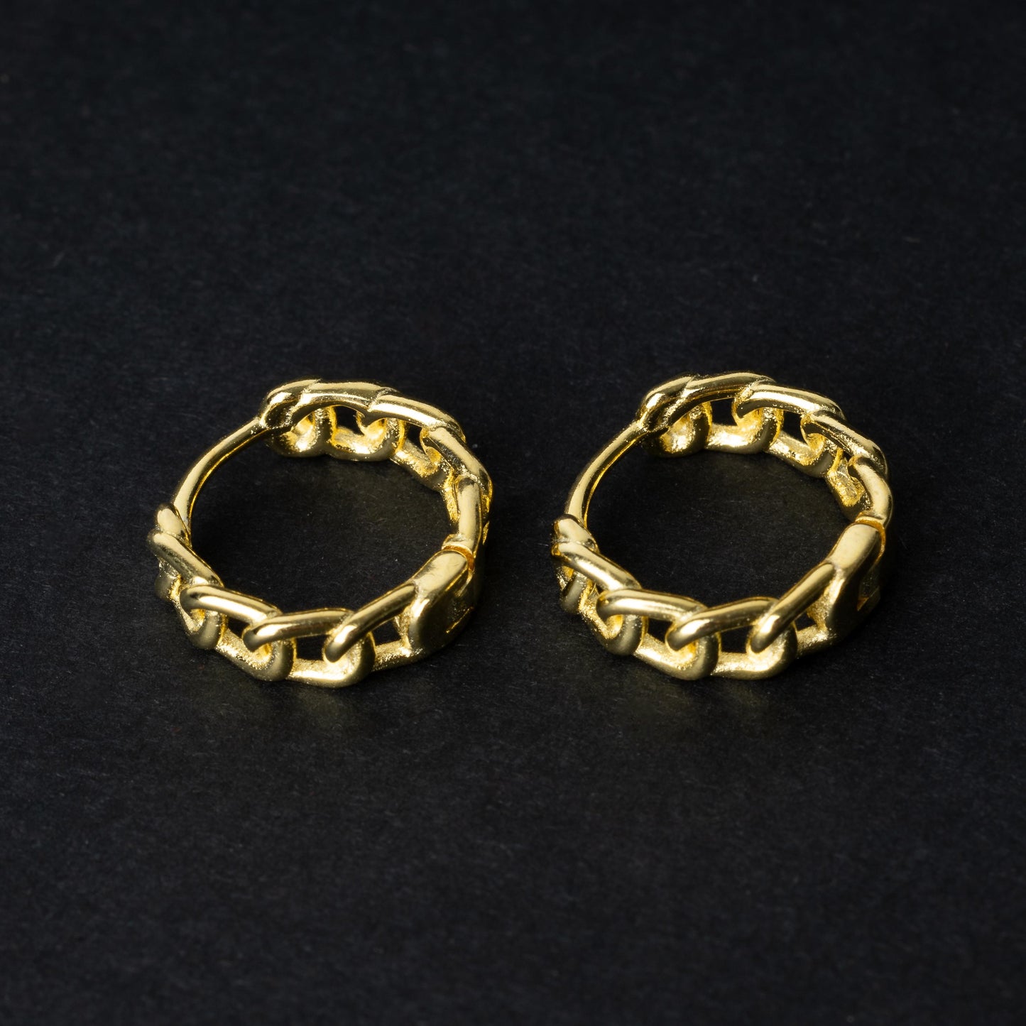 Gold hoop earrings with a chain-link design, displayed on a dark background.
