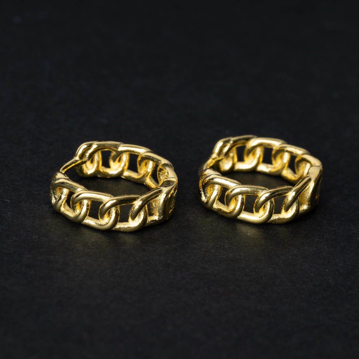Gold hoop earrings with a chain-link design, displayed on a dark background.