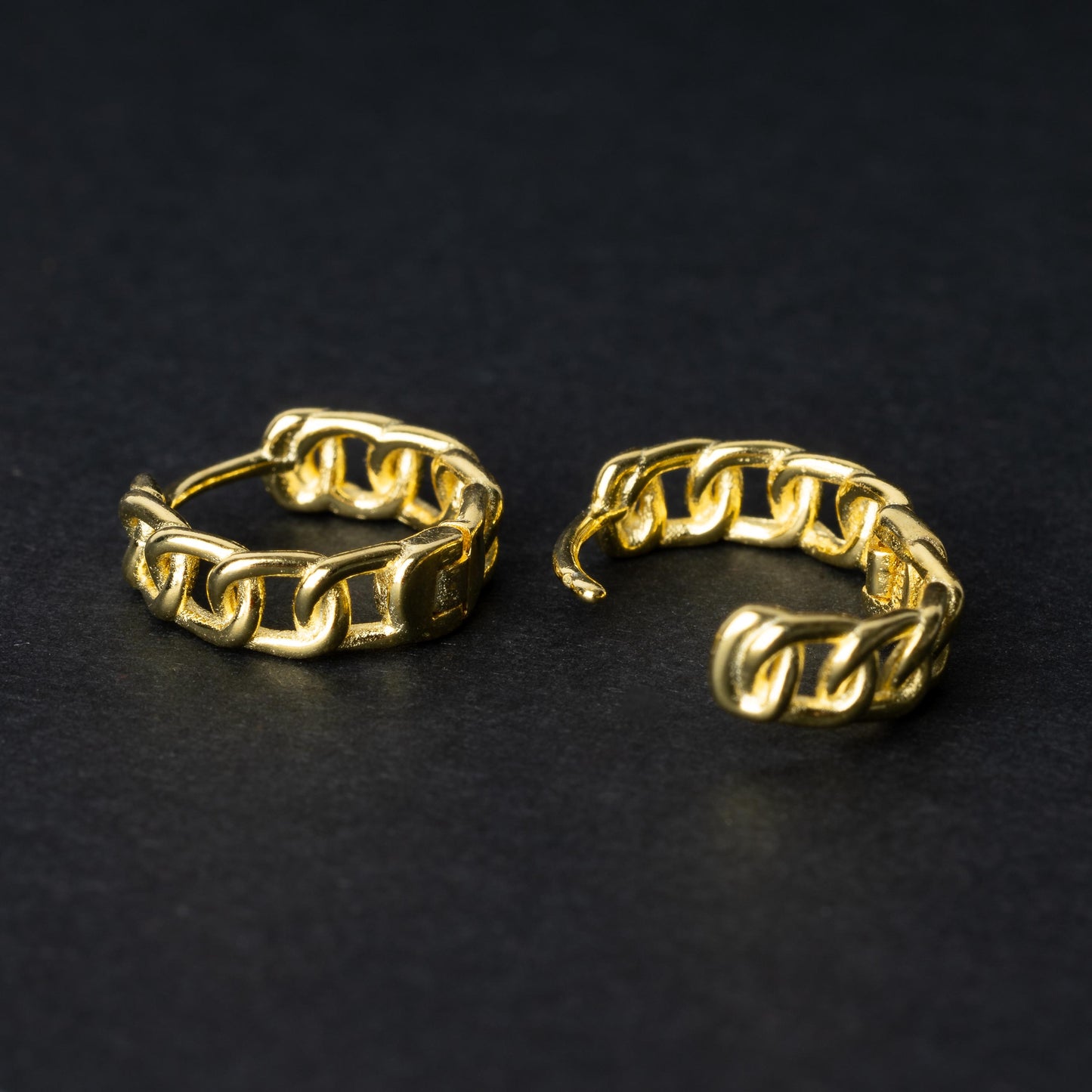 Gold hoop earrings with a chain-link design, displayed on a dark background.