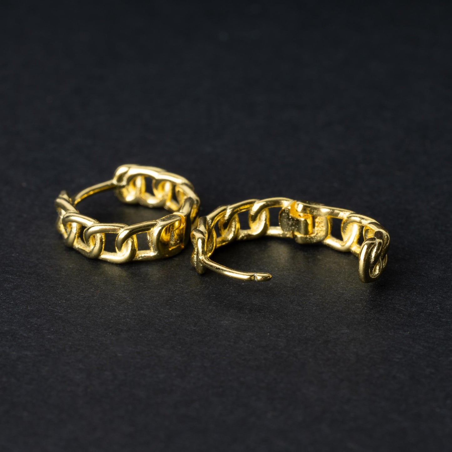Gold hoop earrings with a chain-link design, displayed on a dark background.