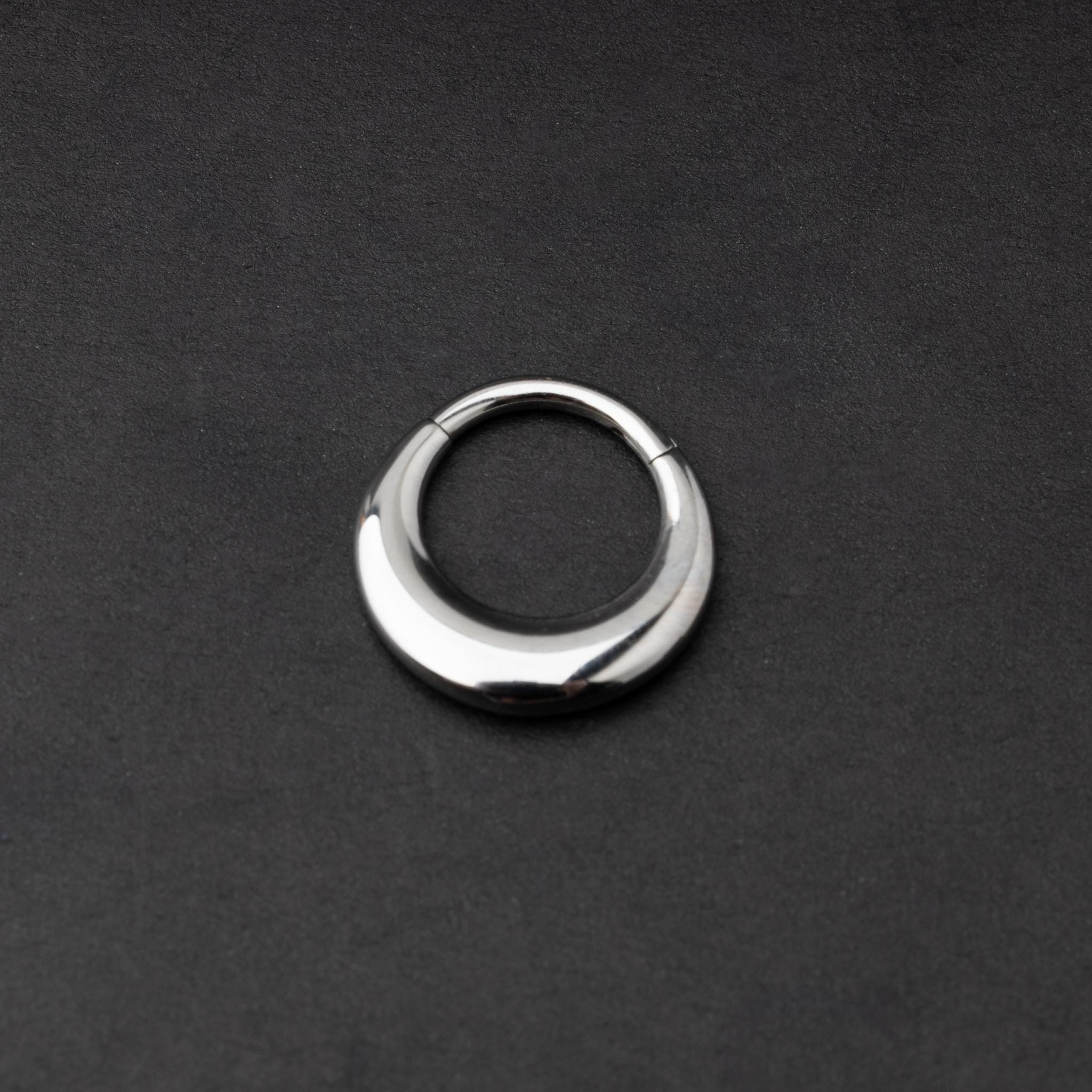 Crescent-shaped septum clicker in silver, with a polished finish, displayed on a dark background.
