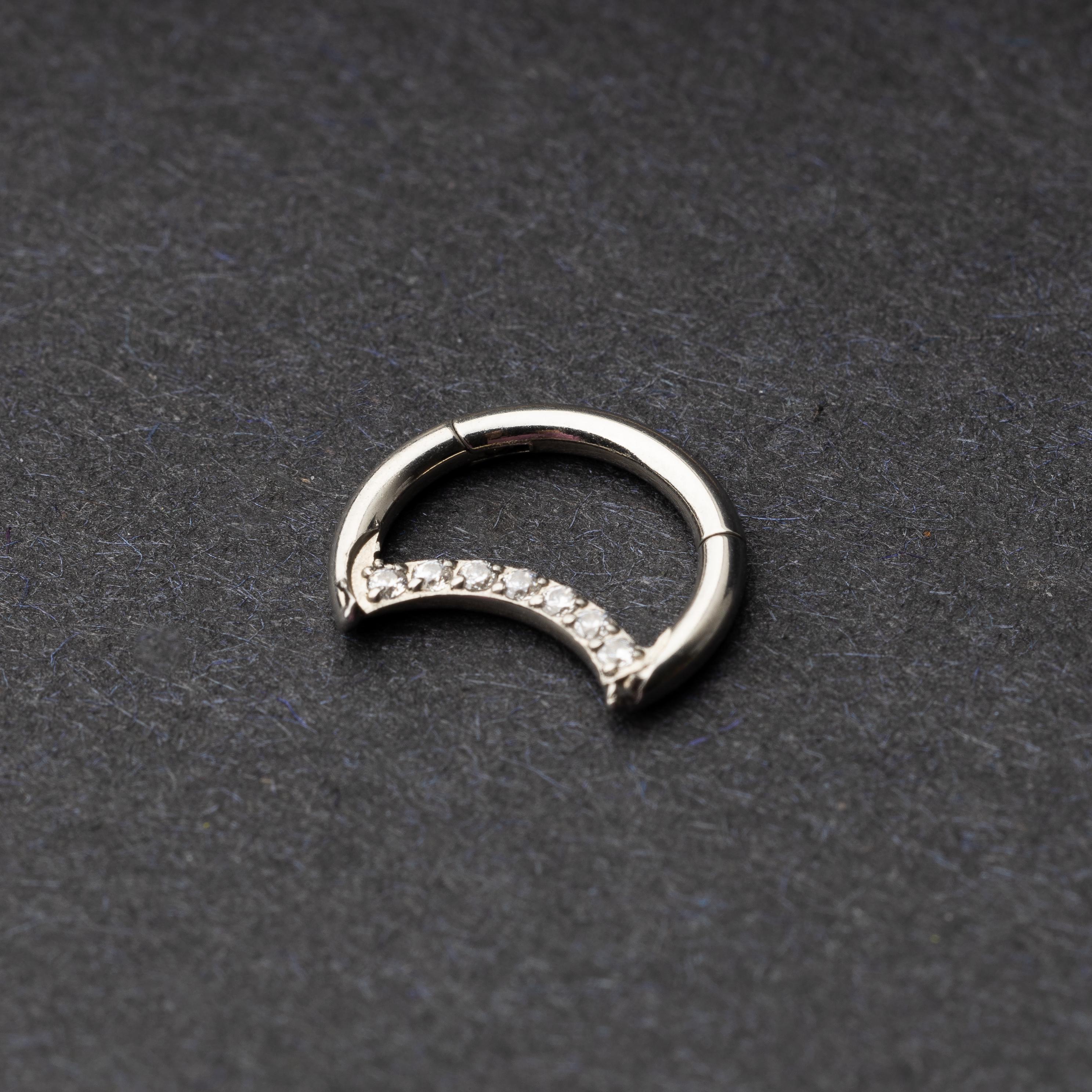 Titanium crescent-shaped clicker with crystal accents along the lower curve, displayed on a dark textured background.
