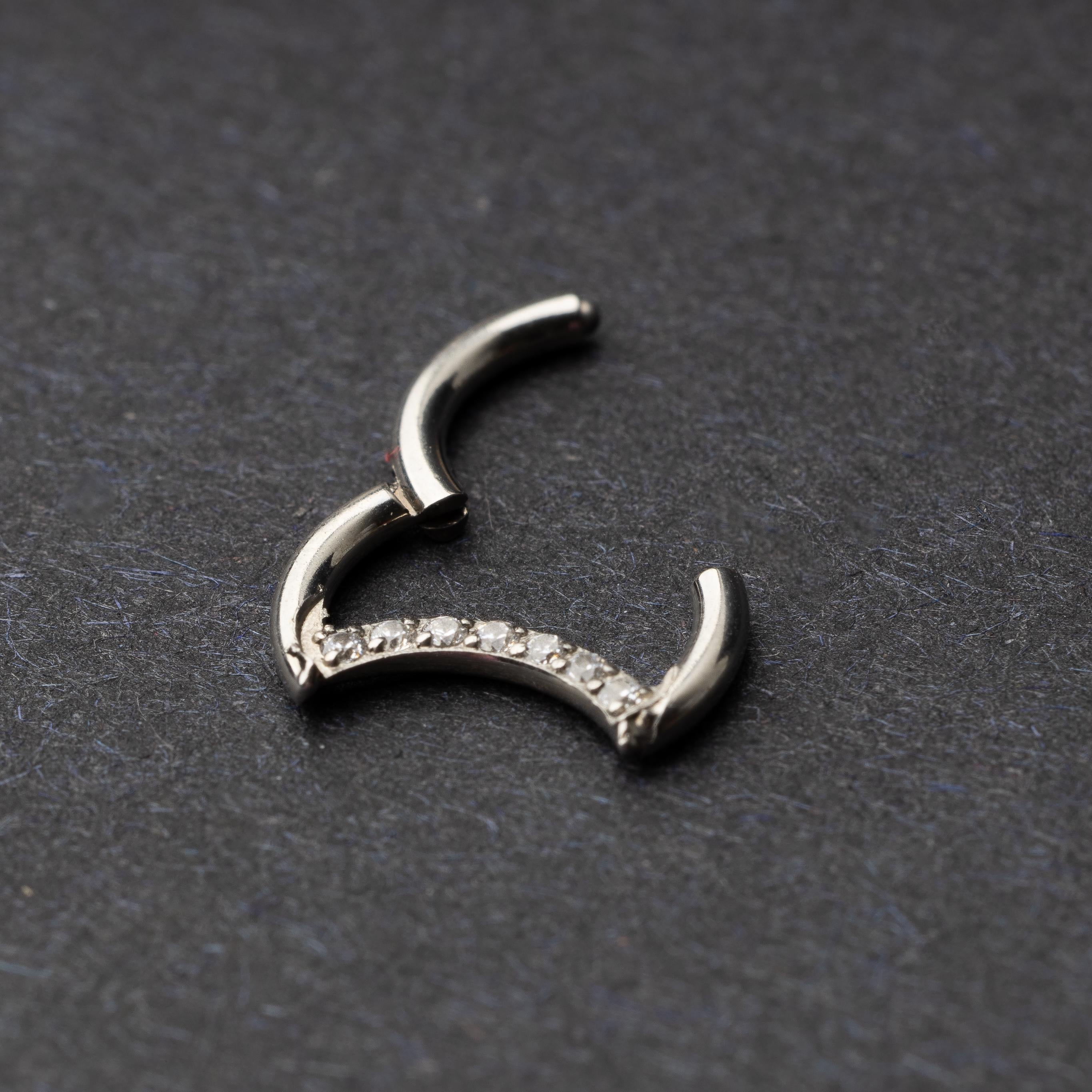 Titanium crescent-shaped clicker with crystal accents along the lower curve, displayed on a dark textured background.