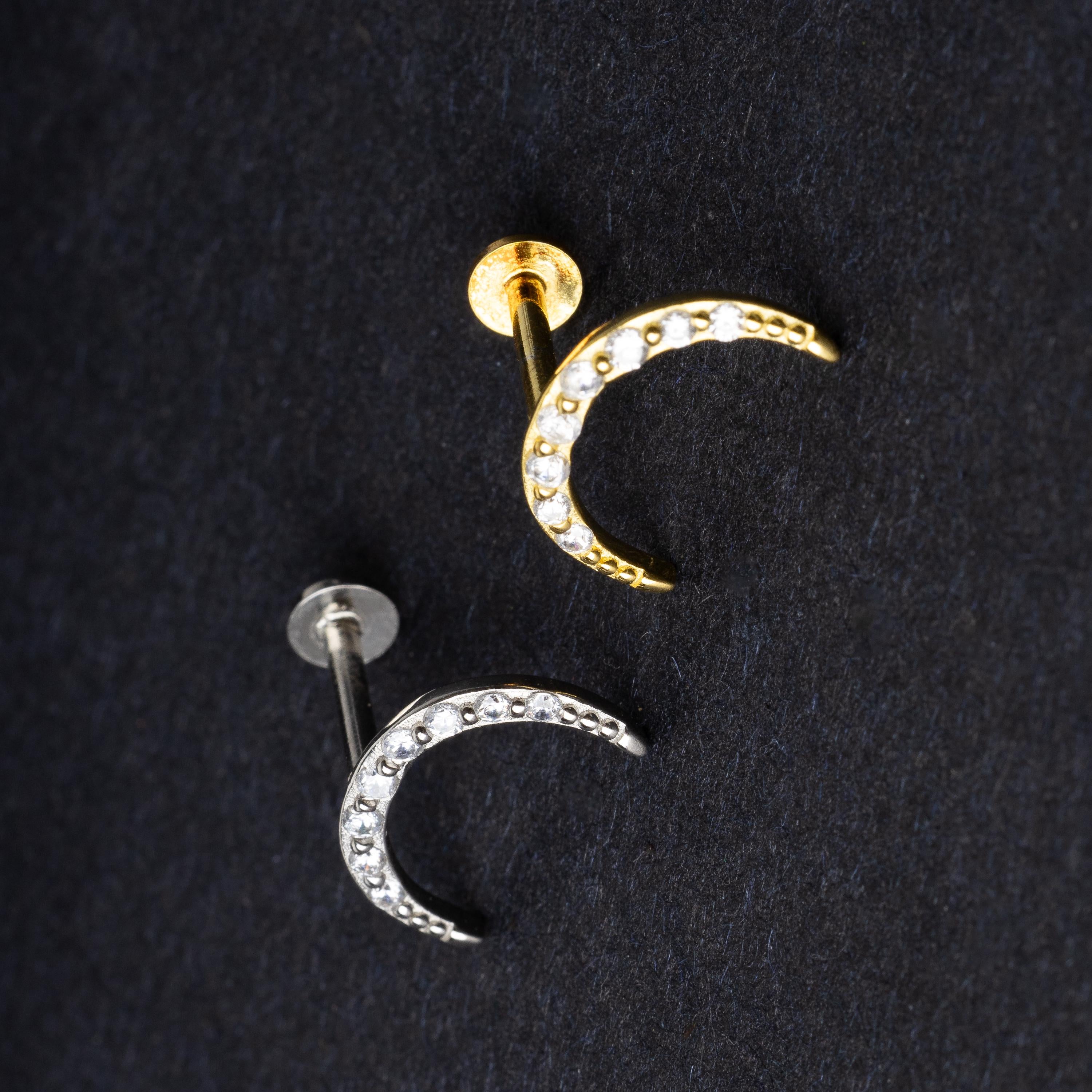 Close-up of gold and silver crescent moon stud earrings featuring CZ gems, displayed on a dark background.