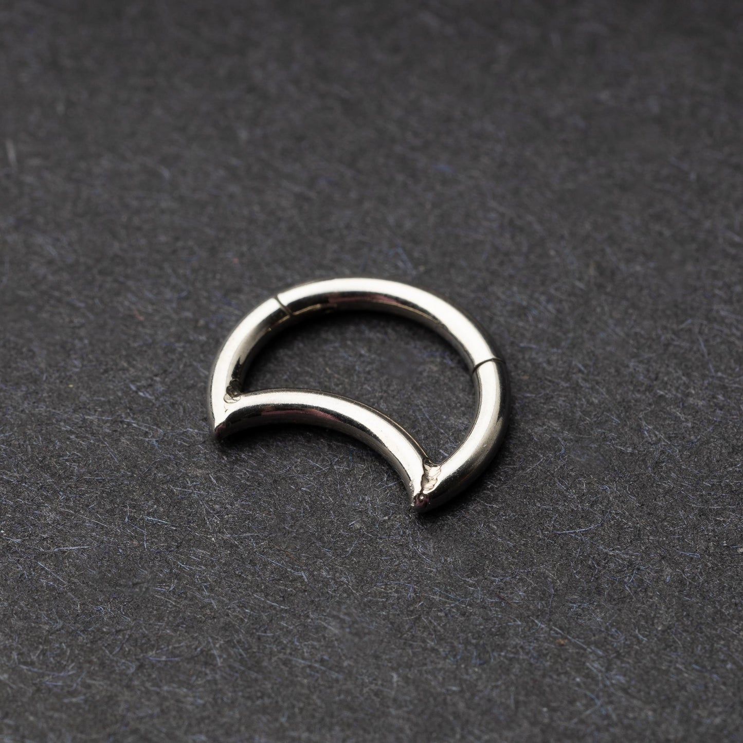 Close-up of a minimalist crescent-shaped clicker made of titanium, displayed on a dark background.