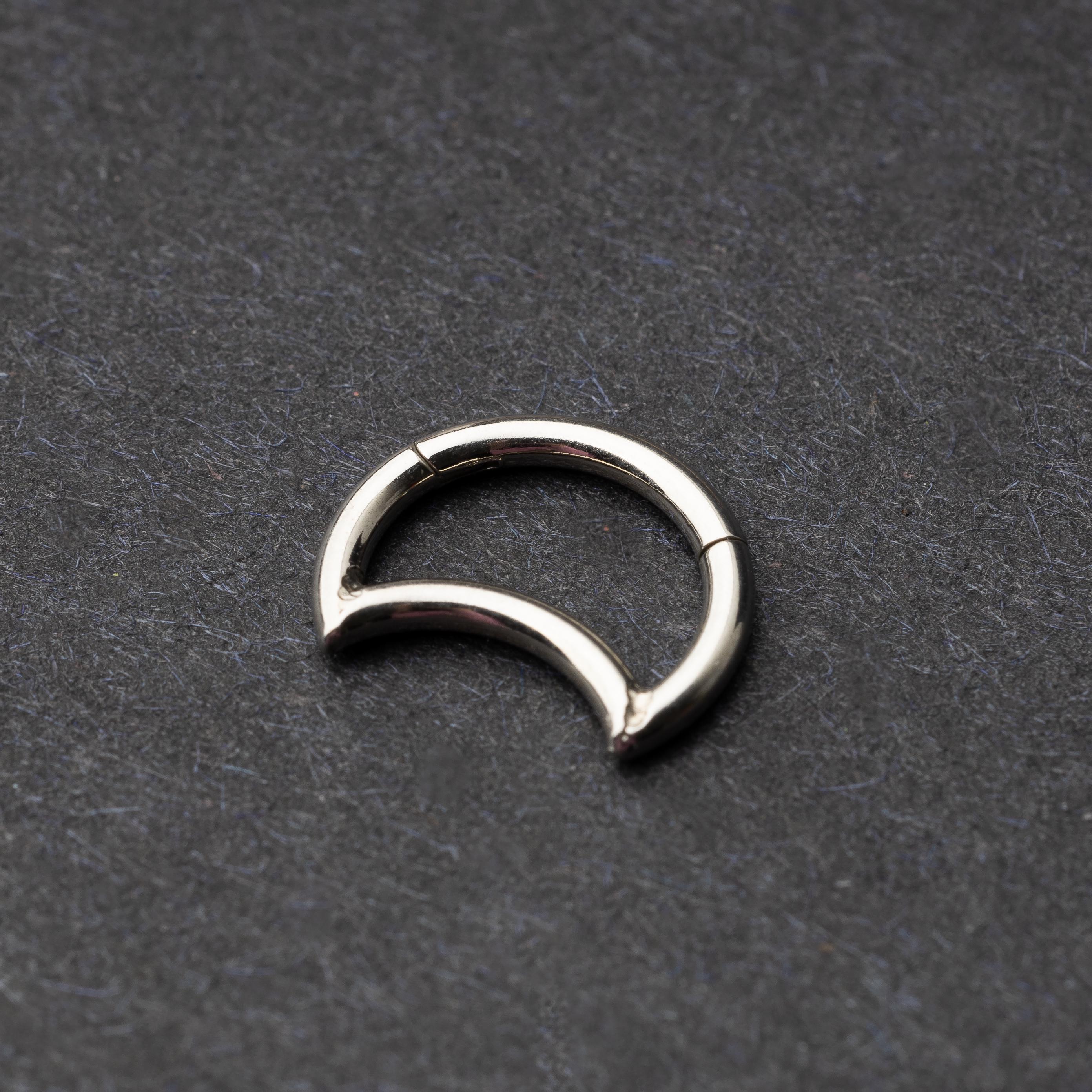 Close-up of a minimalist crescent-shaped clicker made of titanium, displayed on a dark background.