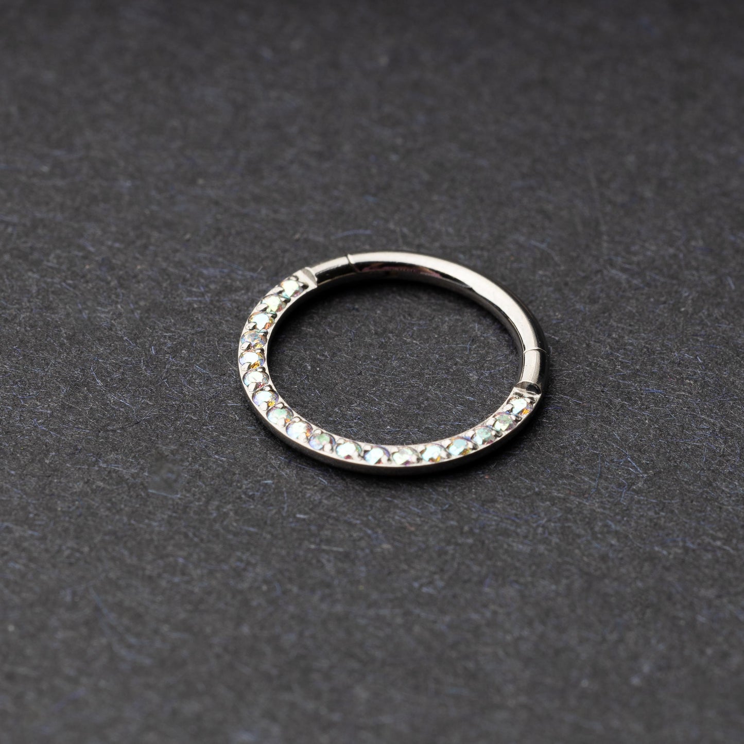 Titanium clicker ring with iridescent crystals, displayed on a dark background.