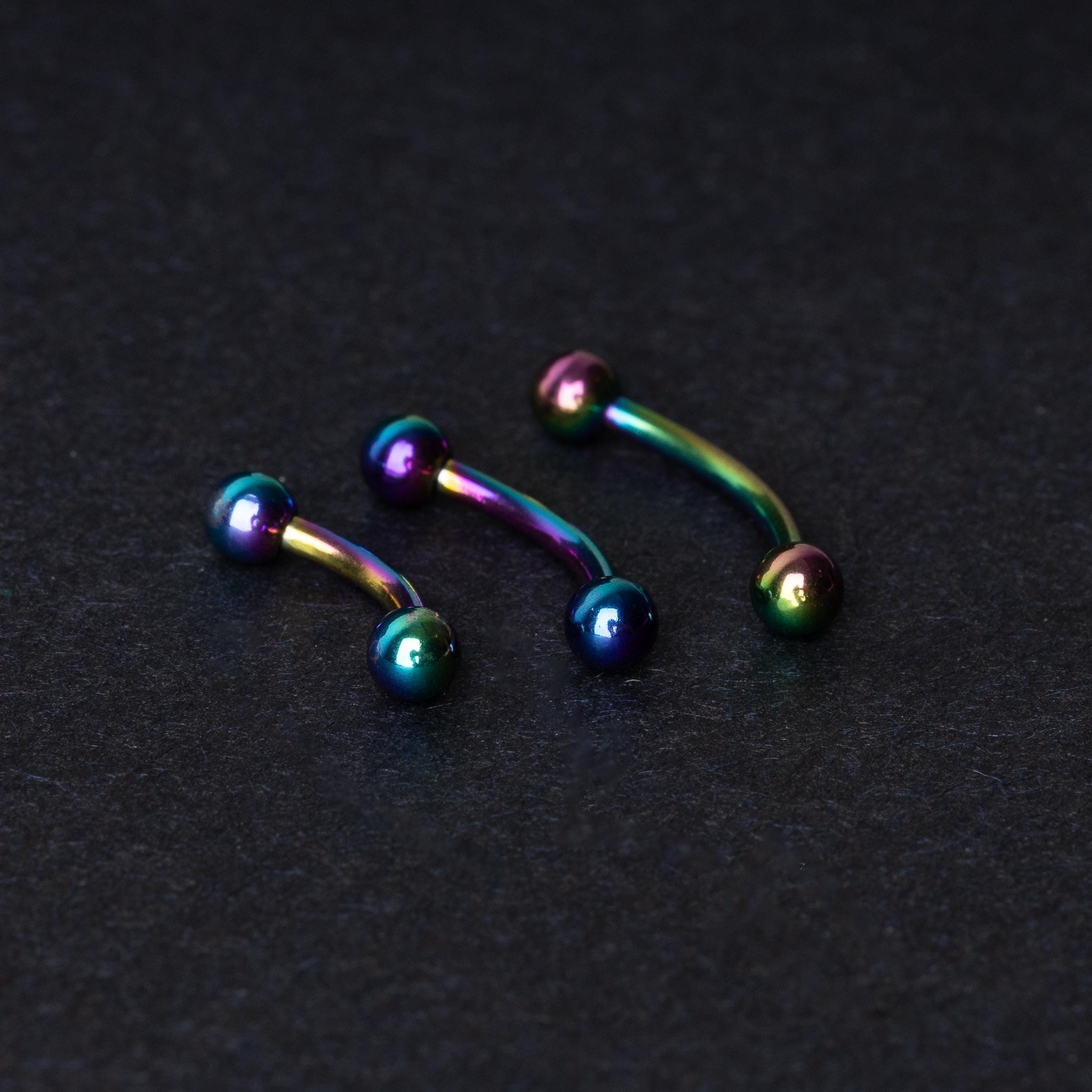 Three curved titanium barbells with a rainbow iridescent finish displayed on a dark textured background, highlighting their vivid colors and smooth finish.