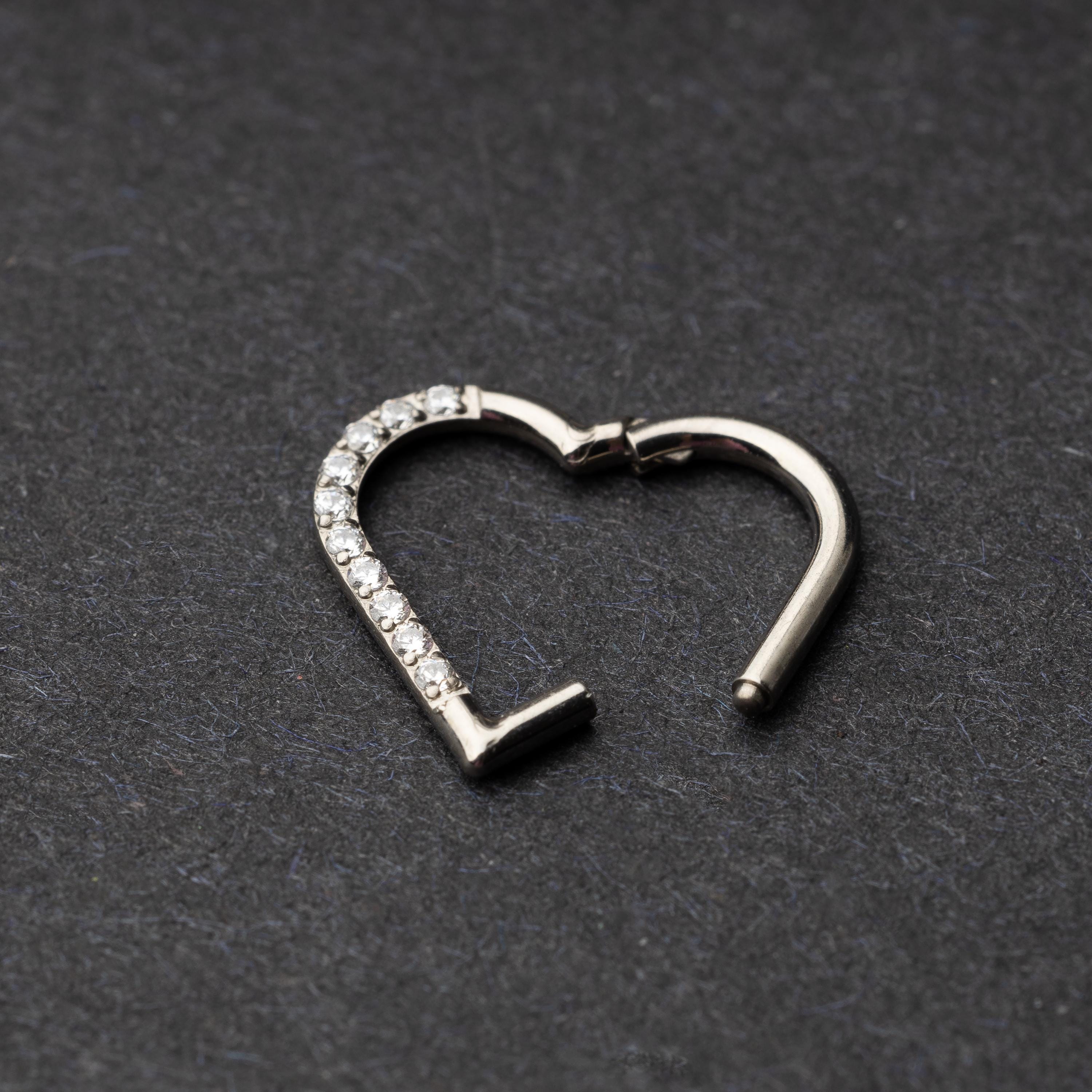 Heart-shaped daith clicker with crystal accents along one side, displayed on a dark textured background.