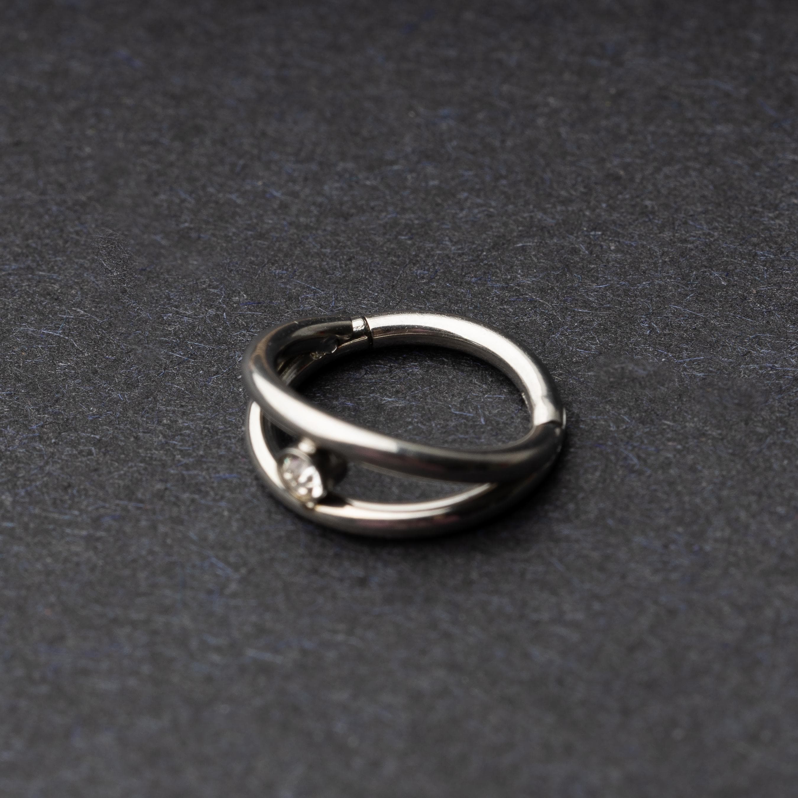 Titanium clicker with a double-layered design and a single cubic zirconia, displayed on a dark background.