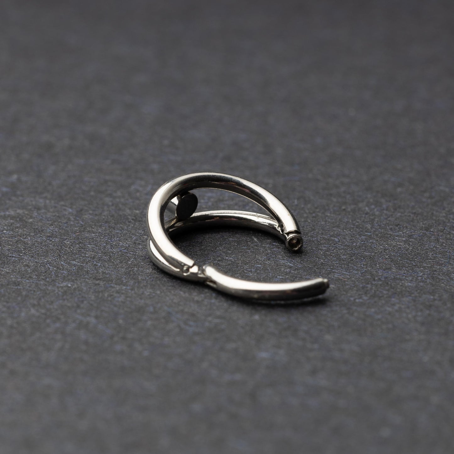 Titanium clicker with a double-layered design and a single cubic zirconia, displayed on a dark background.