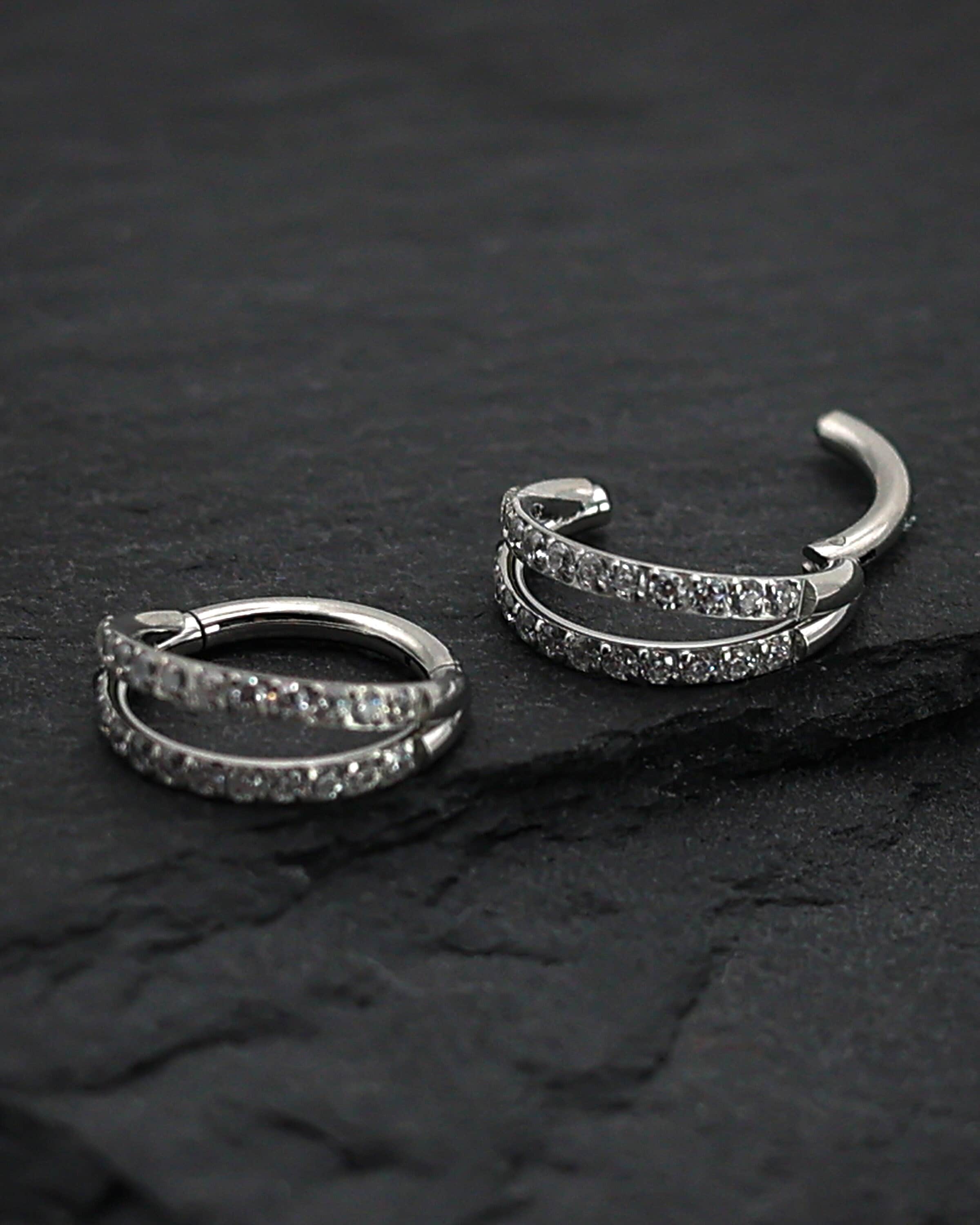 Titanium double-row clickers with cubic zirconia accents, displayed on a textured dark background.
