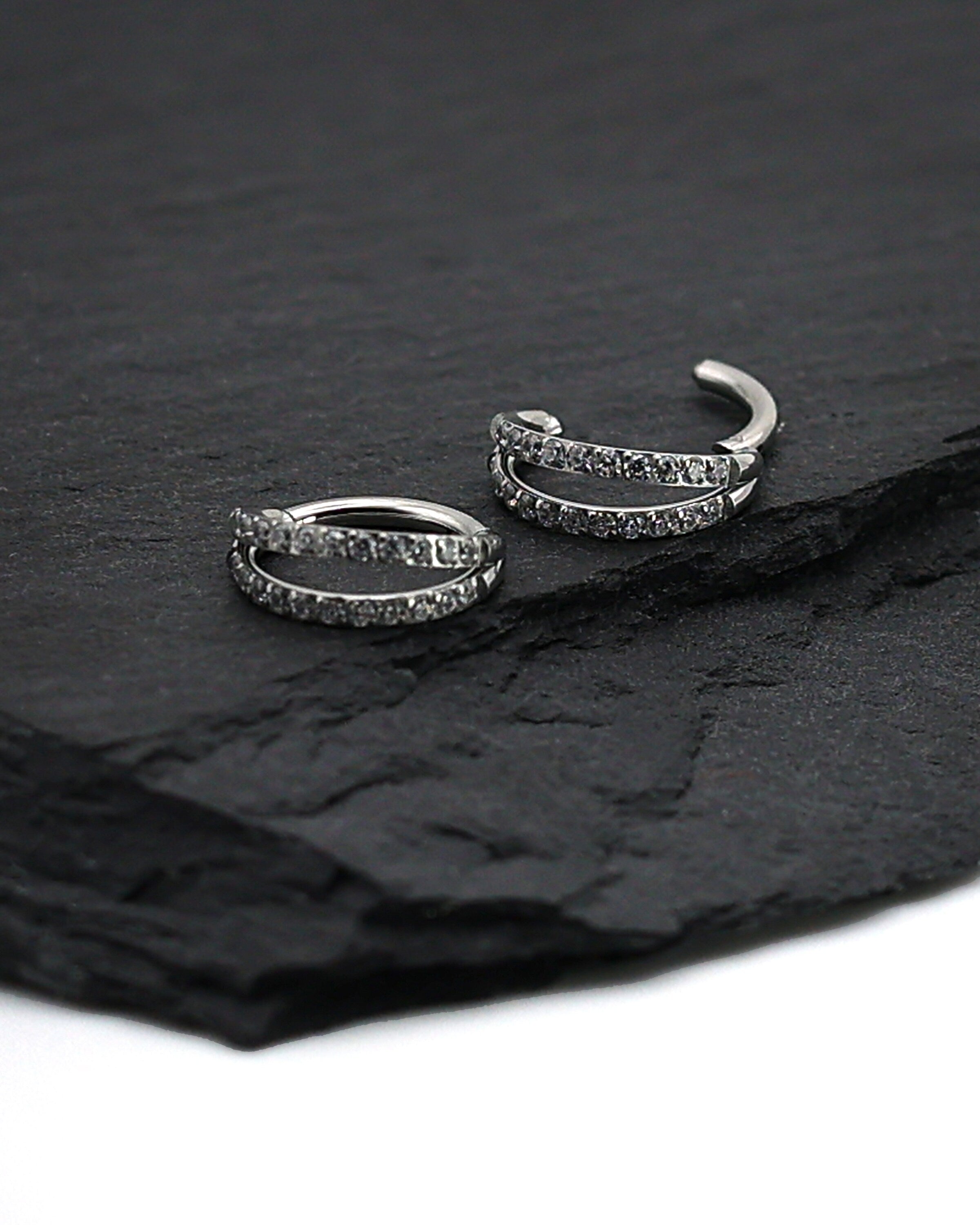 Titanium double-row clickers with cubic zirconia accents, displayed on a textured dark background.