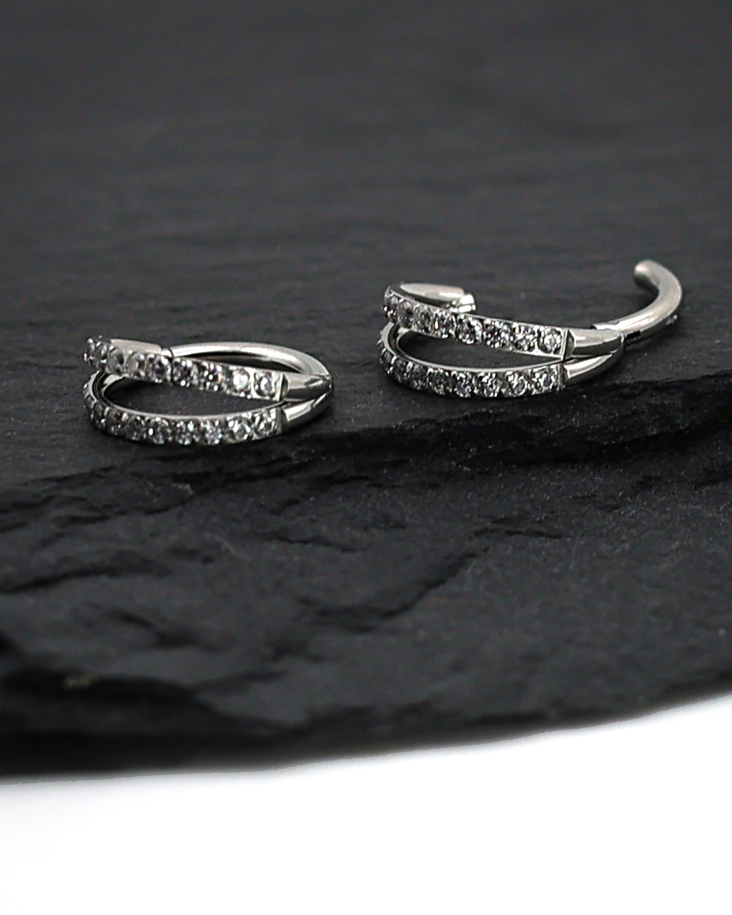 Titanium double-row clickers with cubic zirconia accents, displayed on a textured dark background.