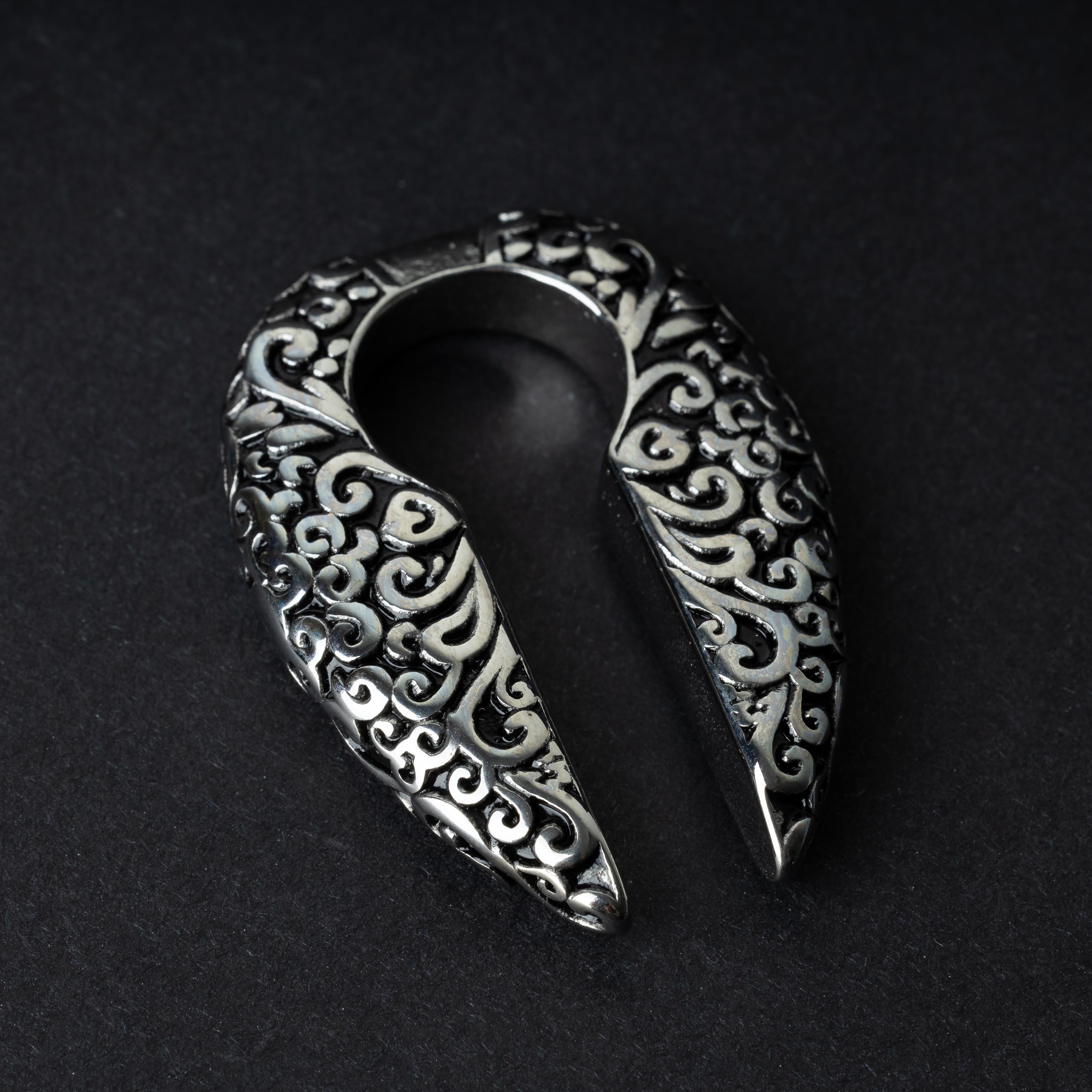 A pair of split ear weights in polished silver with detailed filigree patterns, displayed on a dark background.